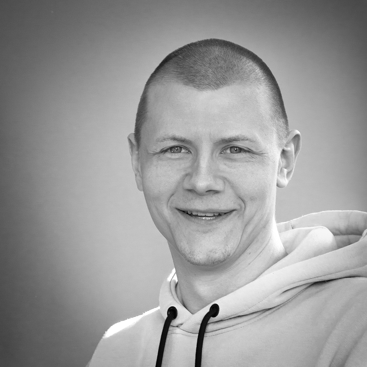Black and white portrait of a smiling person wearing a hoodie.