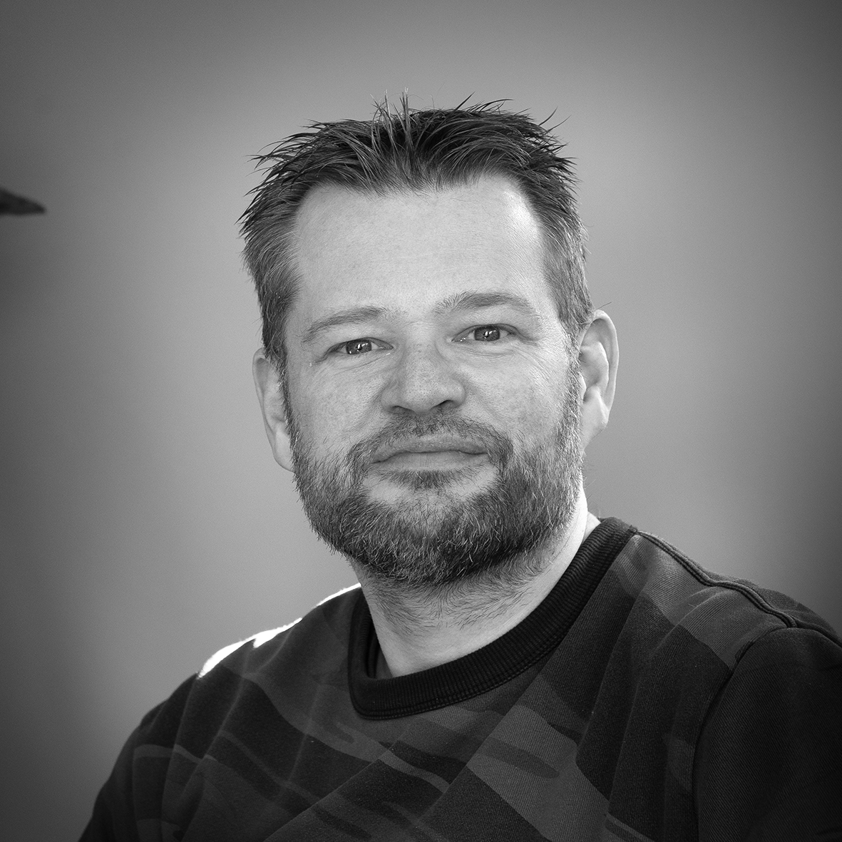 Black and white portrait of a man with a beard, wearing a patterned shirt.