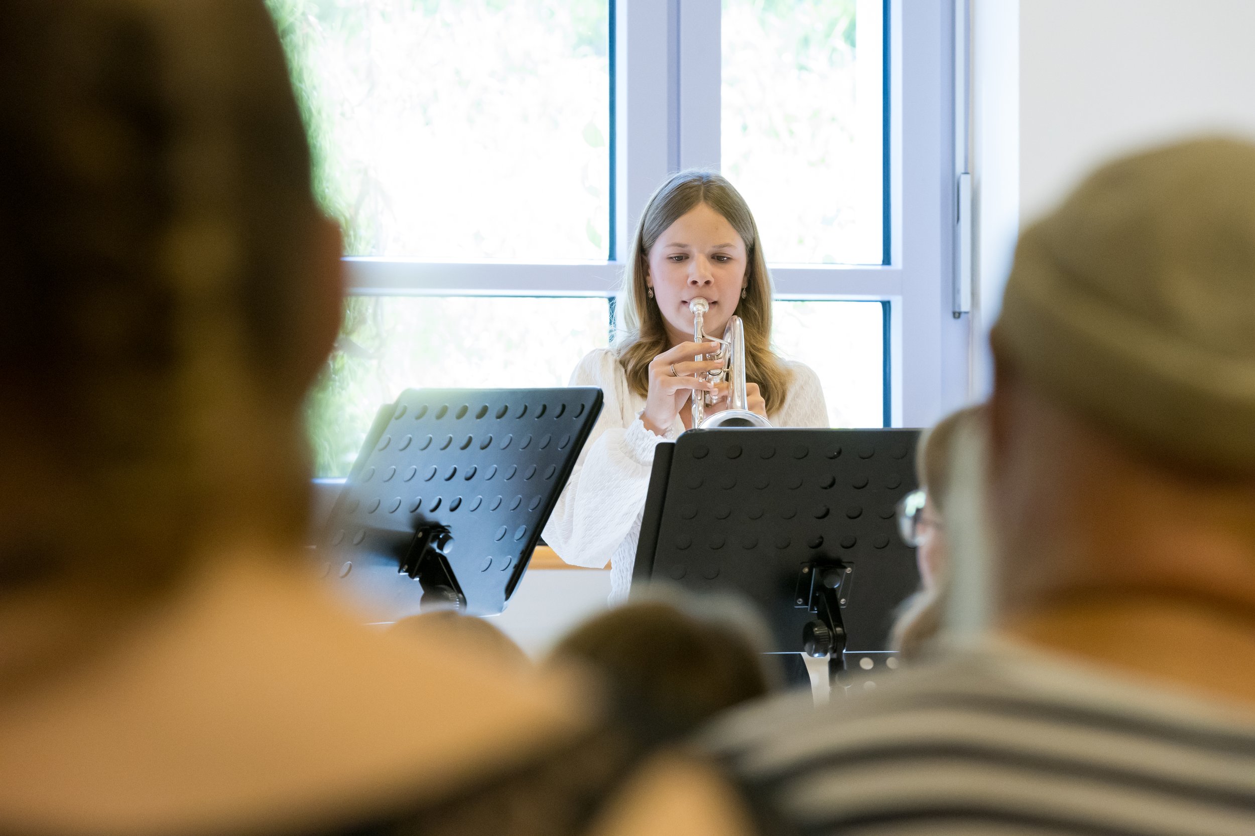Junge Frau spielt Trompete während eines Konzerts vor Publikum in einem Raum mit großen Fenstern.