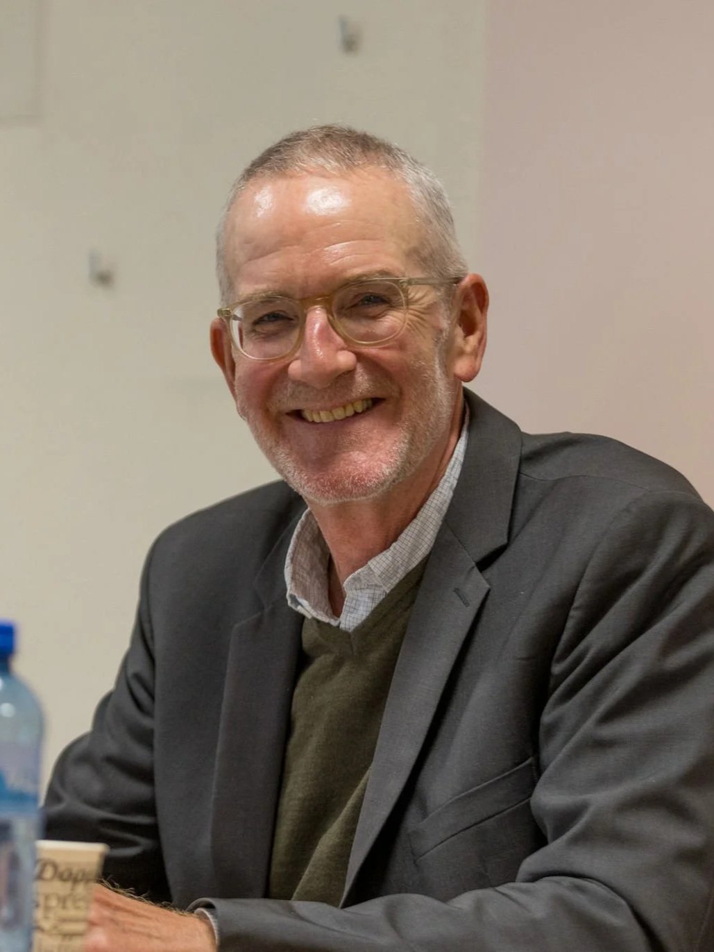 Schwarz-weiß Porträt eines lächelnden Mannes mit Brille und Hemd, gegen hellen Hintergrund.