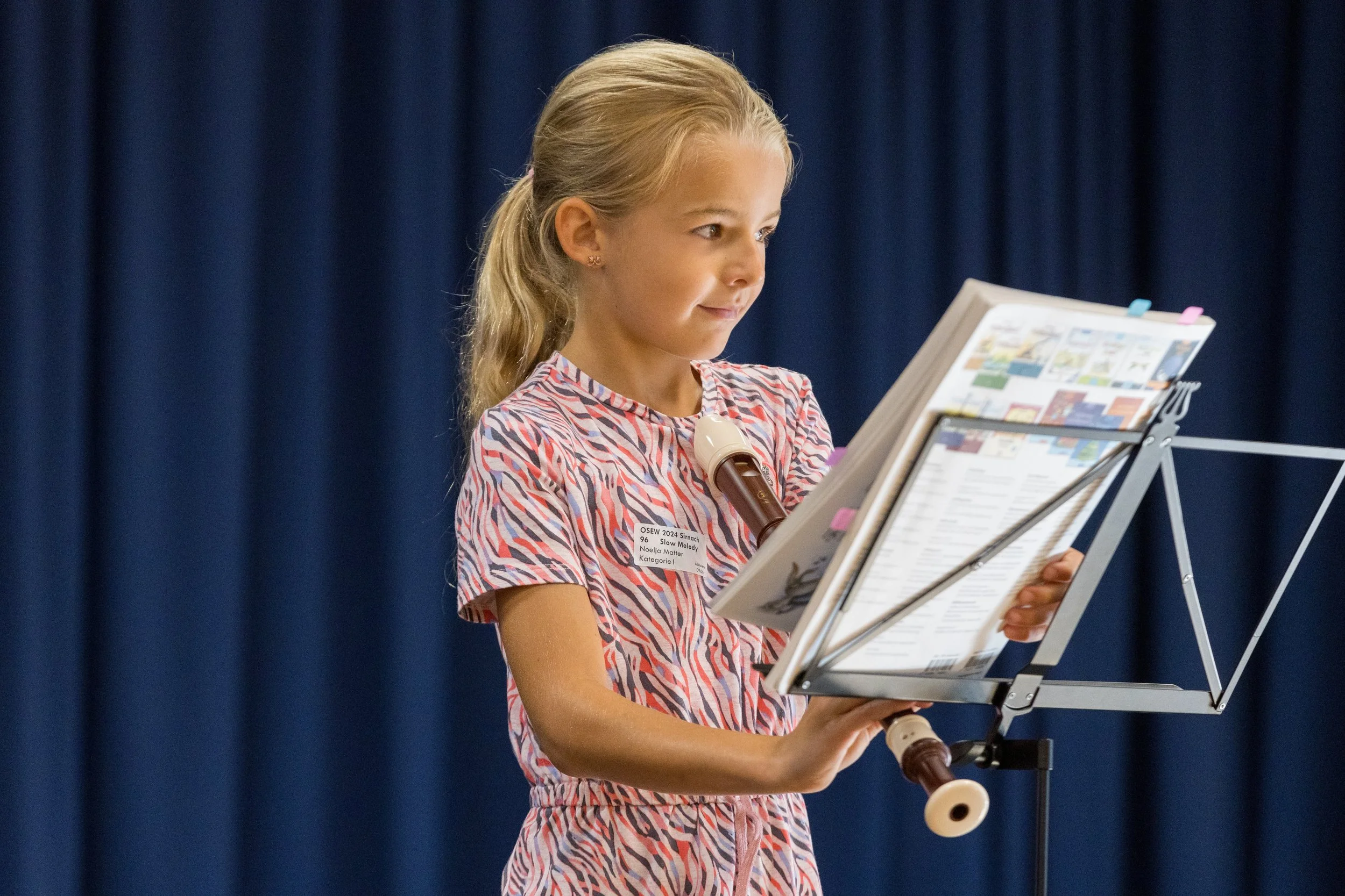 Junge singt bei einem Musikcontest, liest Noten auf einer Notenständer, hinter ihr ein blauer Vorhang.
