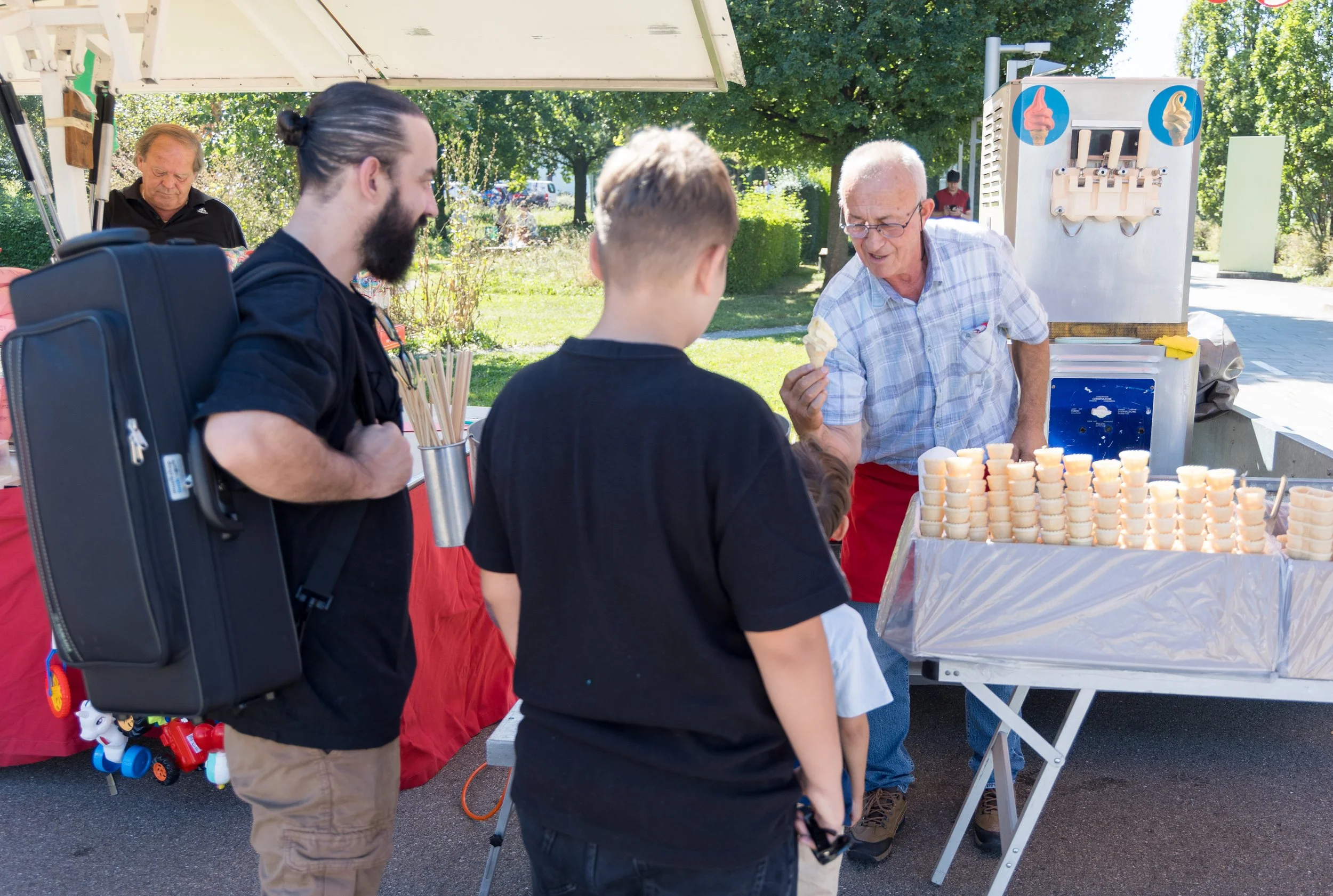 Eisverkäufer verkauft Eiswaffeln an drei Kunden, darunter zwei Kinder, bei einem Outdoor-Event an einem sonnigen Tag.