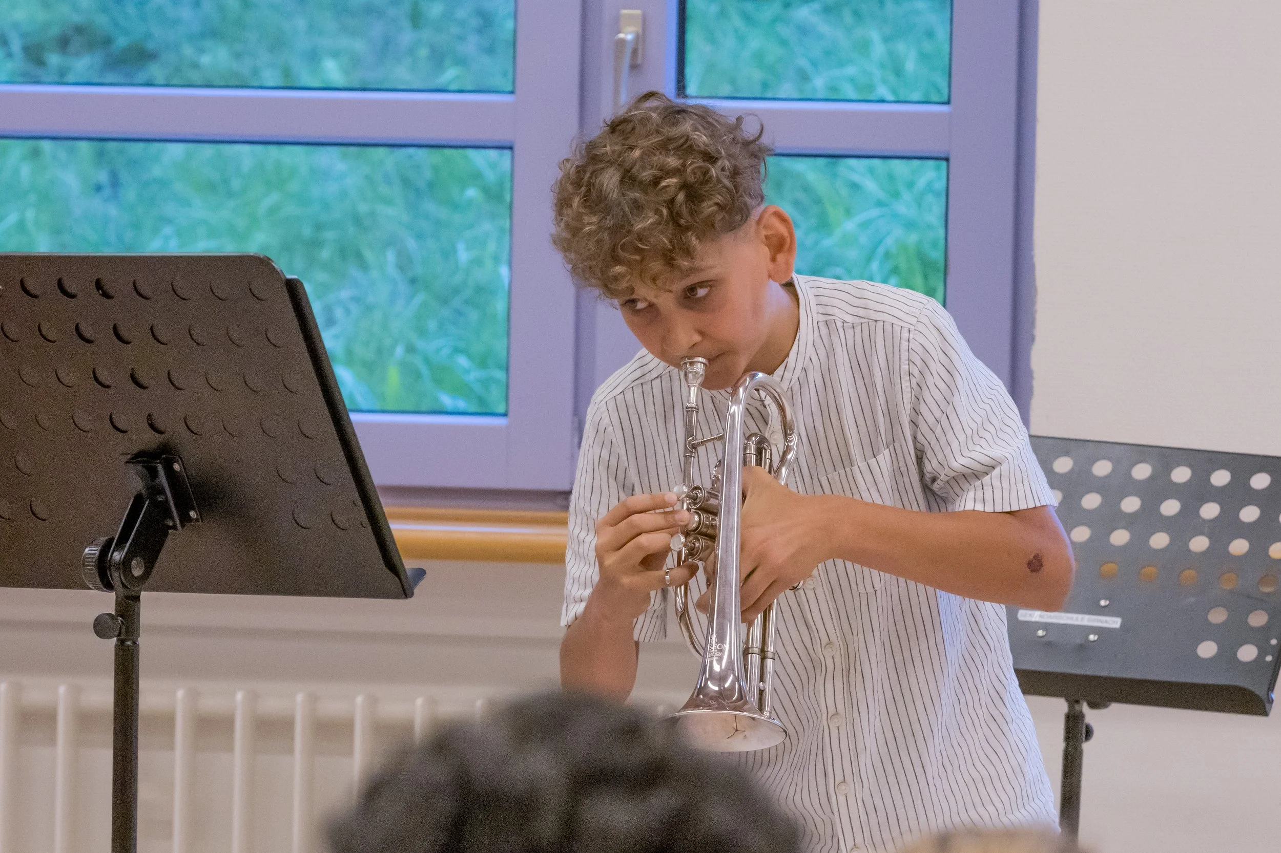 Ein Junge mit lockigem Haar spielt auf einer Trompete in einem Musikraum.
