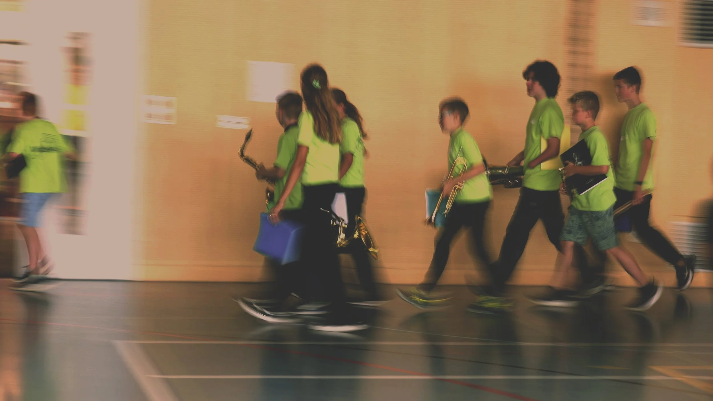 Junge Menschen in grünen T-Shirts laufen durch eine Halle, einige tragen Musikinstrumente.