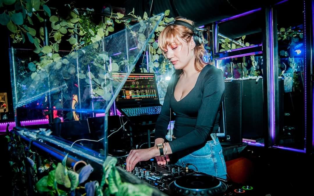DJ som spiller musikk i en klubb med lys og planter rundt seg.
