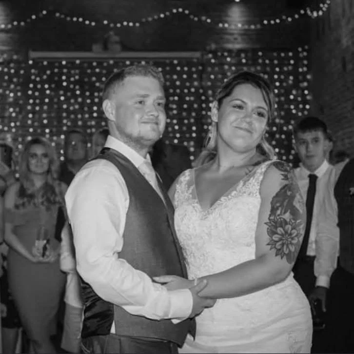 Black and white photo of a bride and groom dancing, surrounded by guests with twinkling lights in the background.