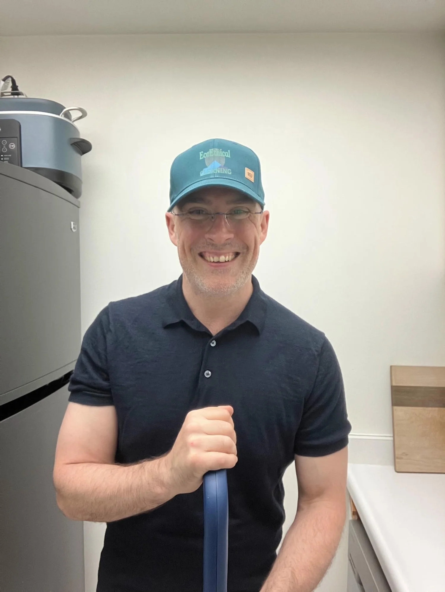 Trevor, wearing a polo shirt and green hat smiling in a kitchen.