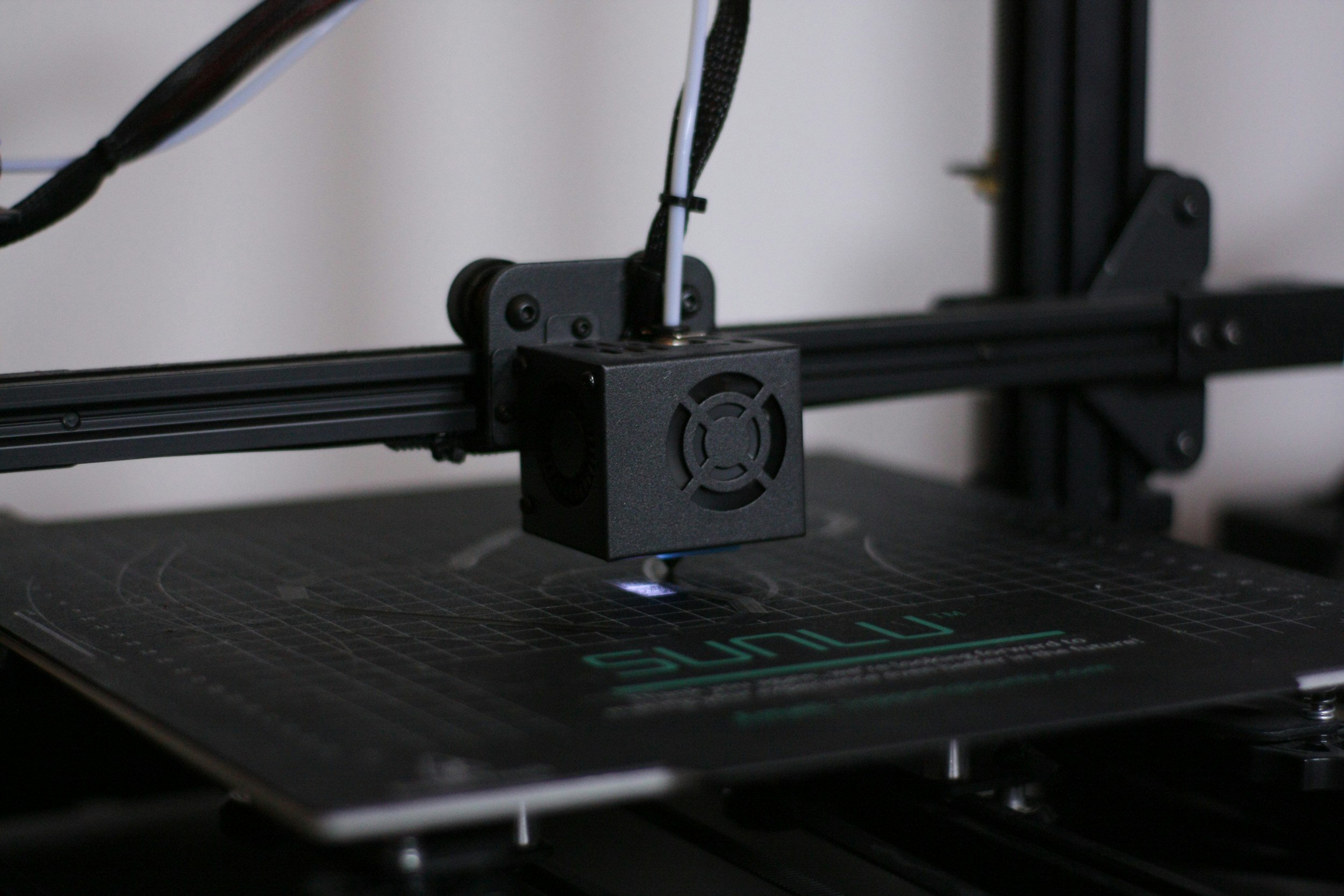 A 3D printer with a black extruder nozzle printing on a platform marked with the brand 'Sunlu'.