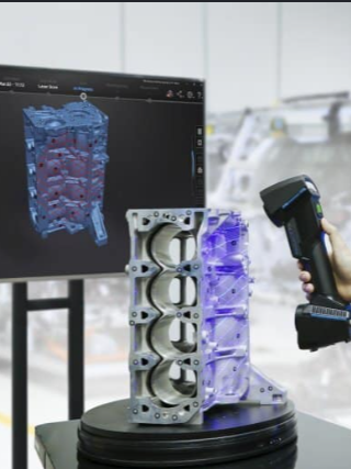 A person using a handheld 3D scanner on an engine component, with a computer monitor displaying a 3D model of the part in the background.