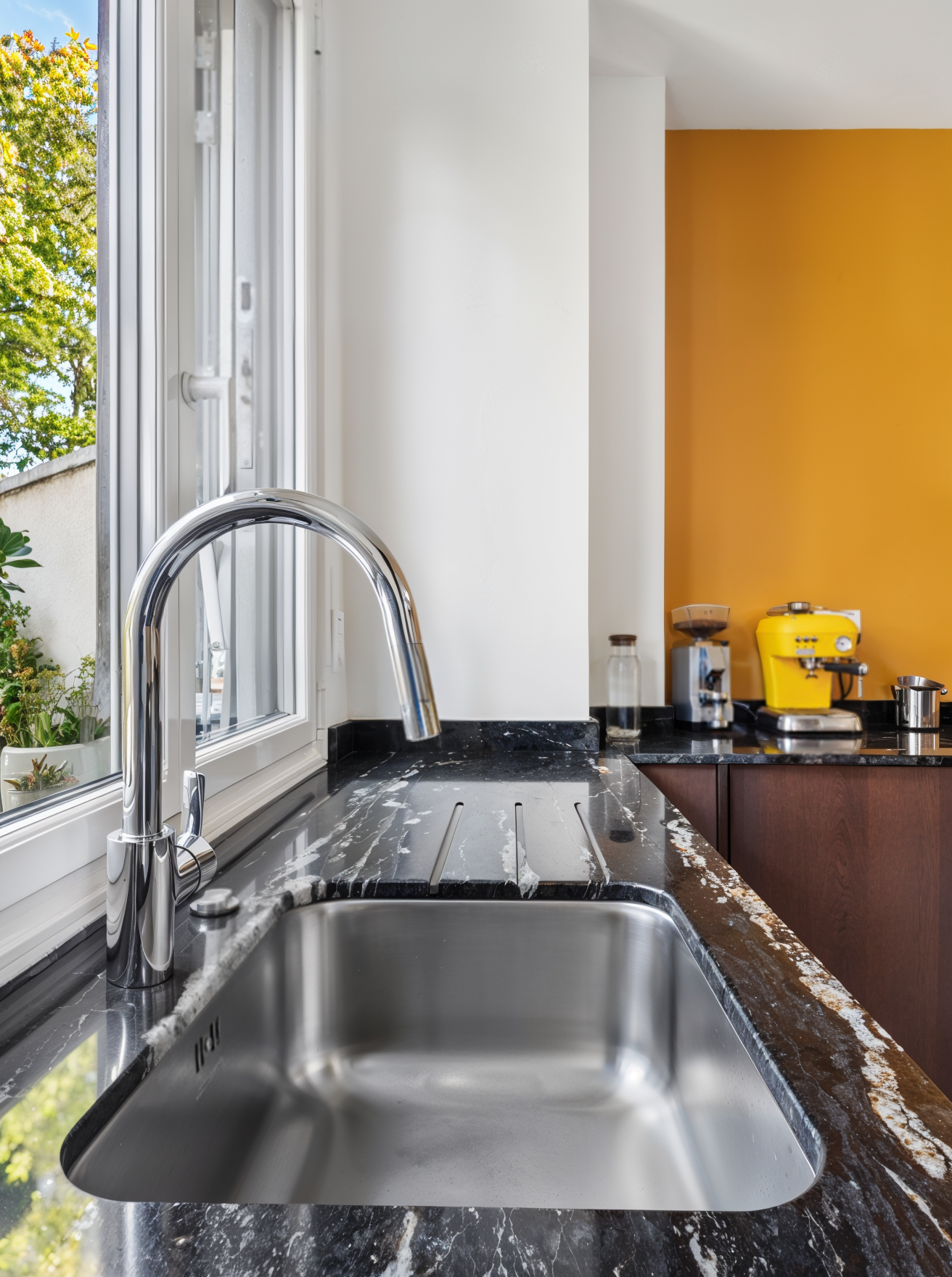 Évier encastré dans un plan de travail en granit noir sur mesure, avec mitigeur chromé et vue sur le jardin.