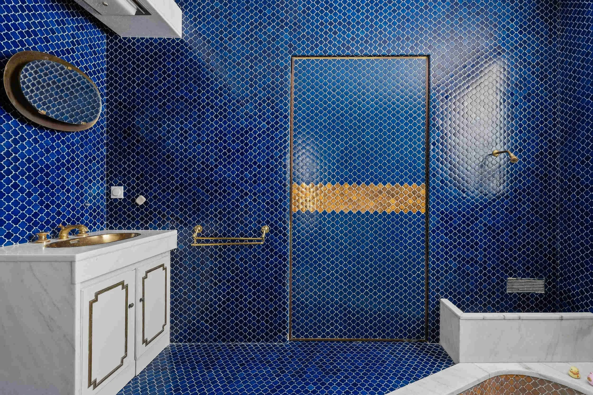 Salle de bains atypique à Colombes avec mosaïque bleue, baignoire maçonnée conservée et robinetterie dorée.