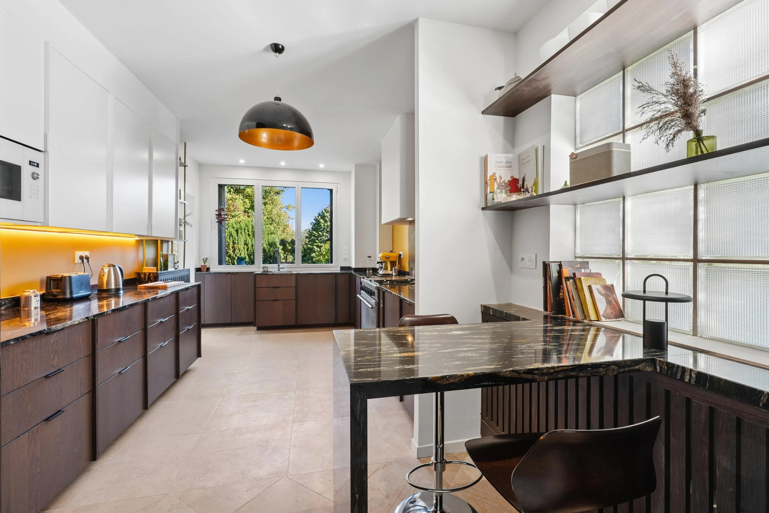 Cuisine sur mesure à Colombes avec façades noyer, plan de travail en granit noir et espace repas intégré.