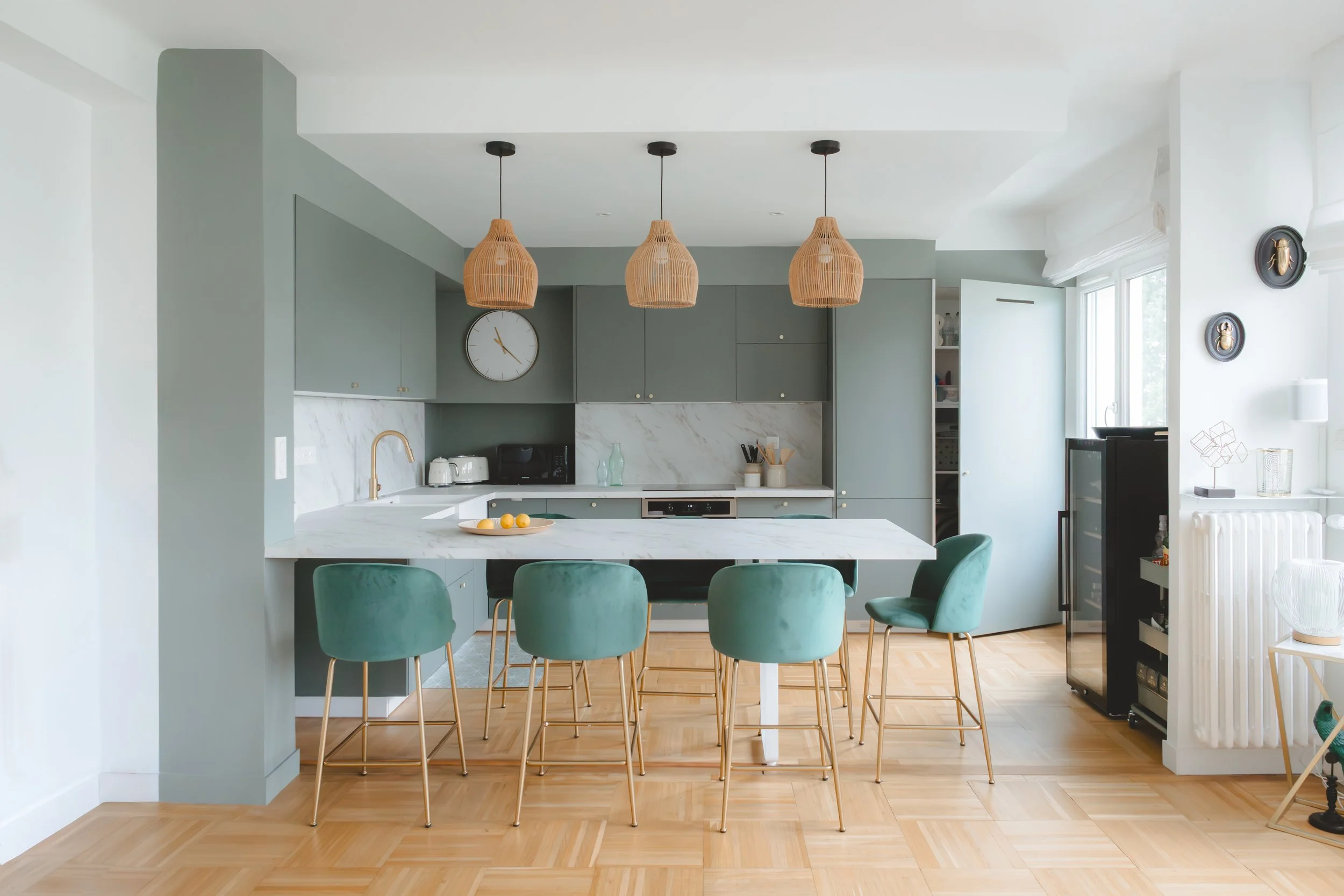 Cuisine ouverte contemporaine à Caen, avec façades vertes mates, plan de travail bois et niches sur mesure. Un projet signé RIVABEL mêlant fonctionnalité et esthétique dans un appartement de 80 m². Porte de la buanderie secrète ouverte.