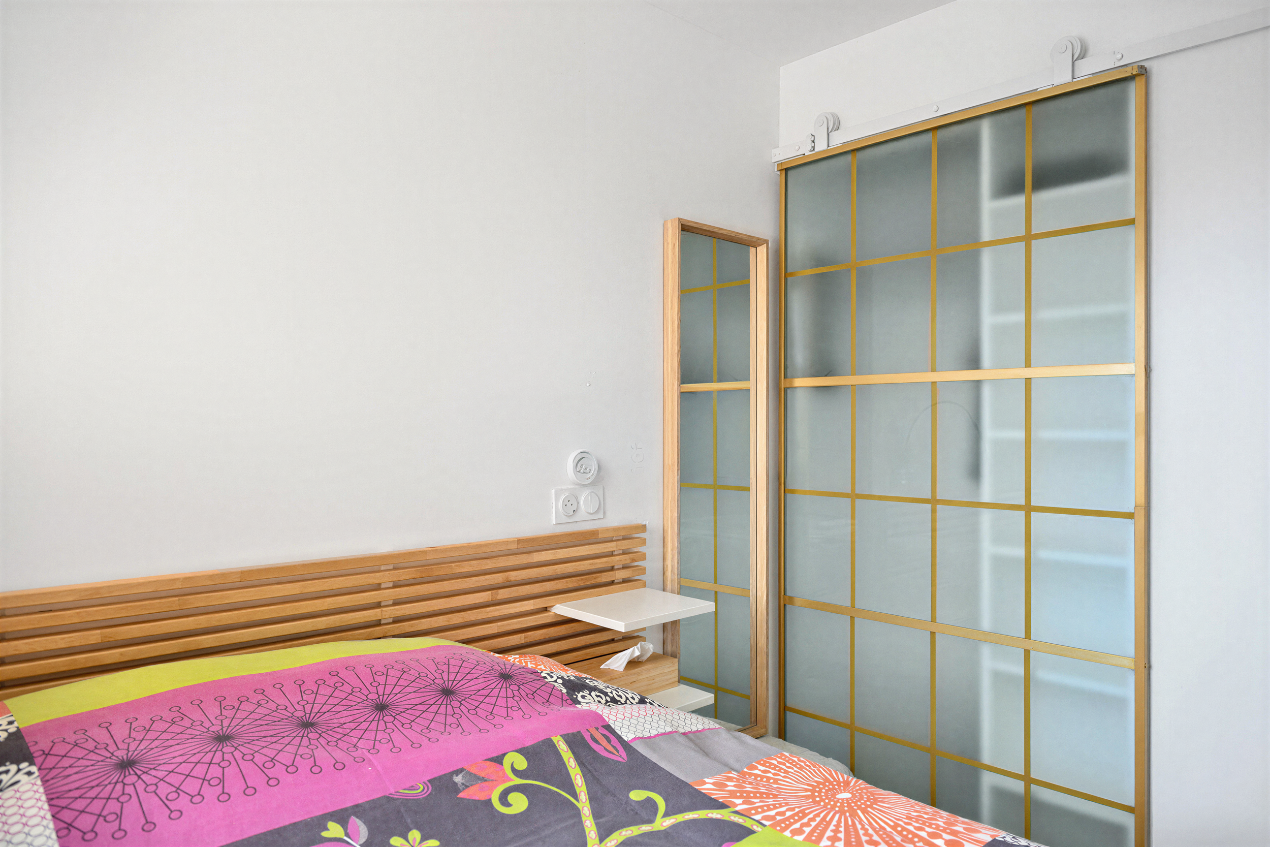 Chambre au style japonisant avec tête de lit en bois et porte coulissante vitrée dans un appartement rénové à Ouistreham.