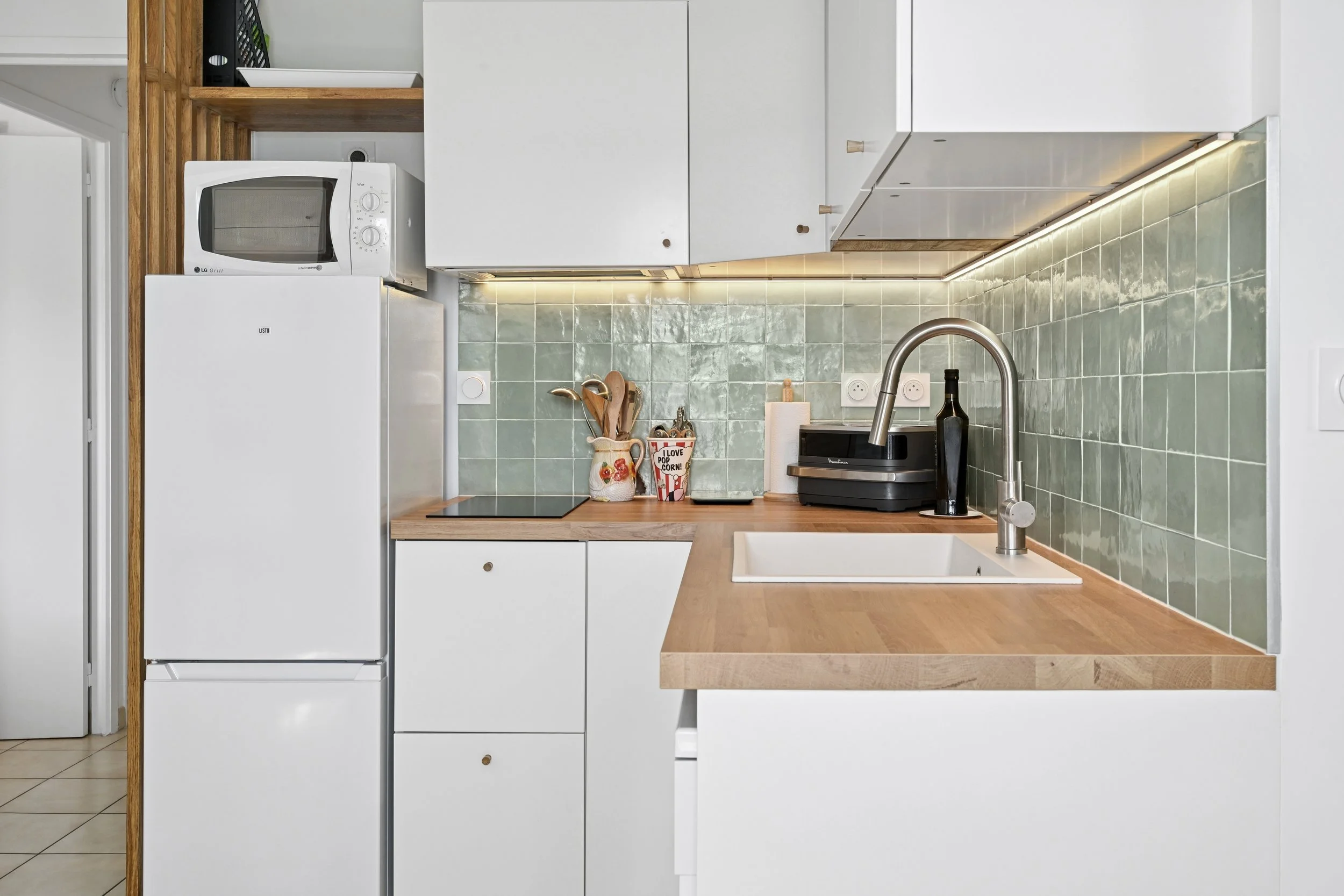 Détail de la cuisine rénovée associant façades blanches, plan de travail en bois et zellige vert sauge.