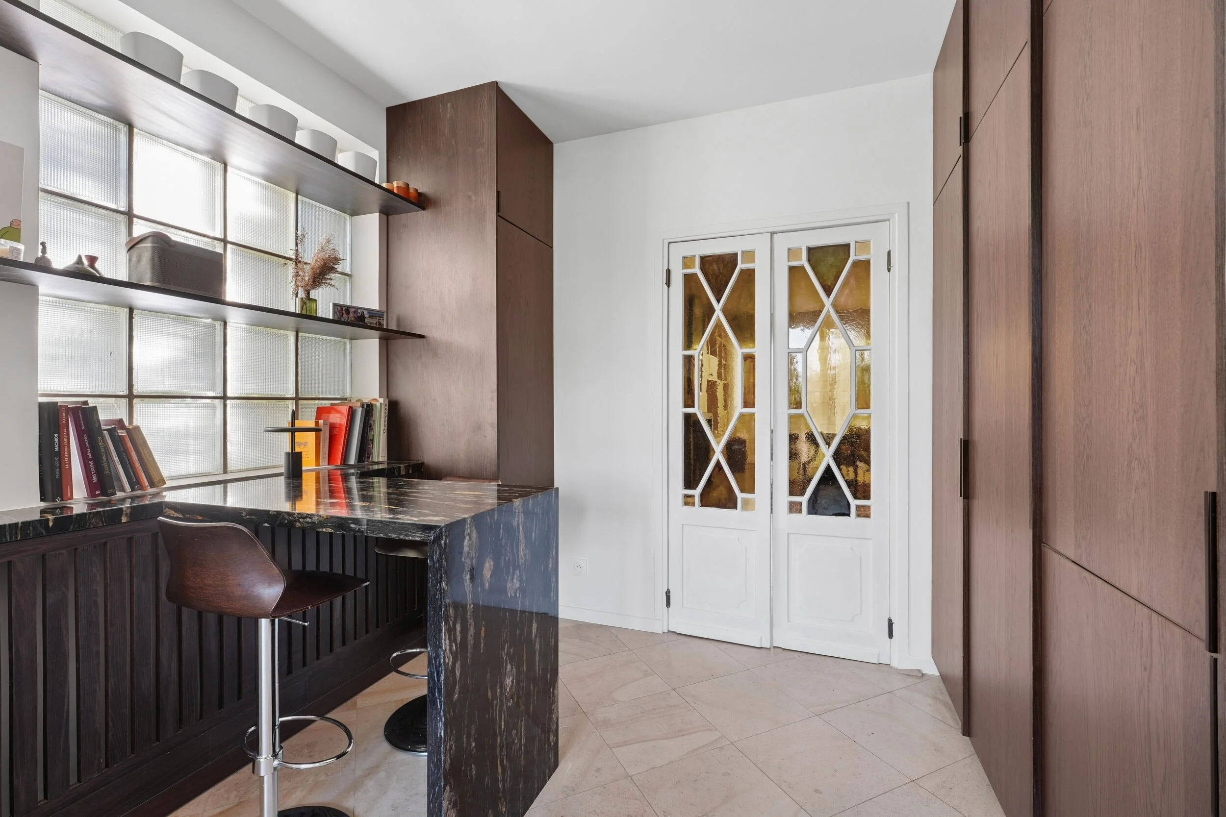 Coin repas en granit sur mesure, rangements en bois foncé et portes anciennes à vitraux conservées dans un appartement à Colombes.