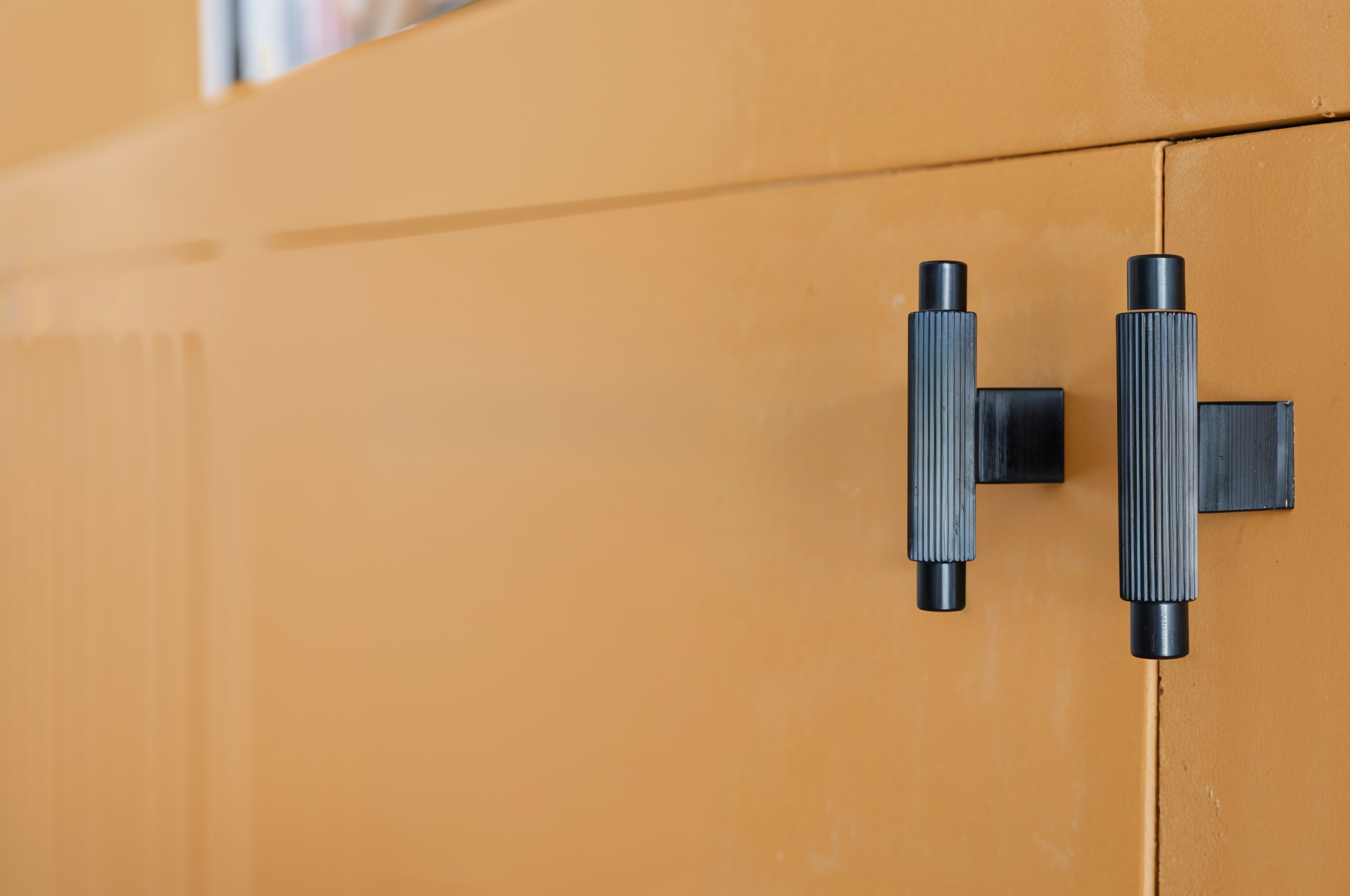 Détail des poignées noires texturées d'un meuble sur mesure ocre, réalisé pour la rénovation d'un appartement à Colombes.