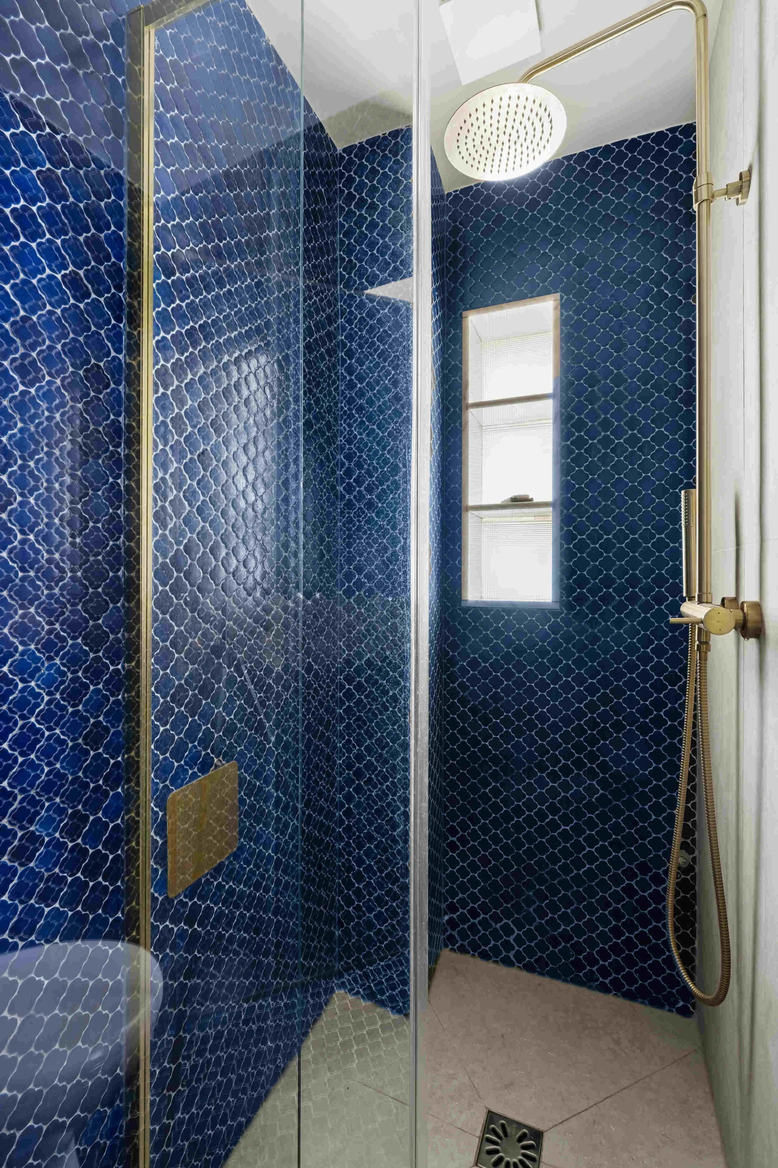 Douche à l'italienne avec mosaïque bleu profond, paroi vitrée et robinetterie dorée dans un appartement rénové à Colombes.