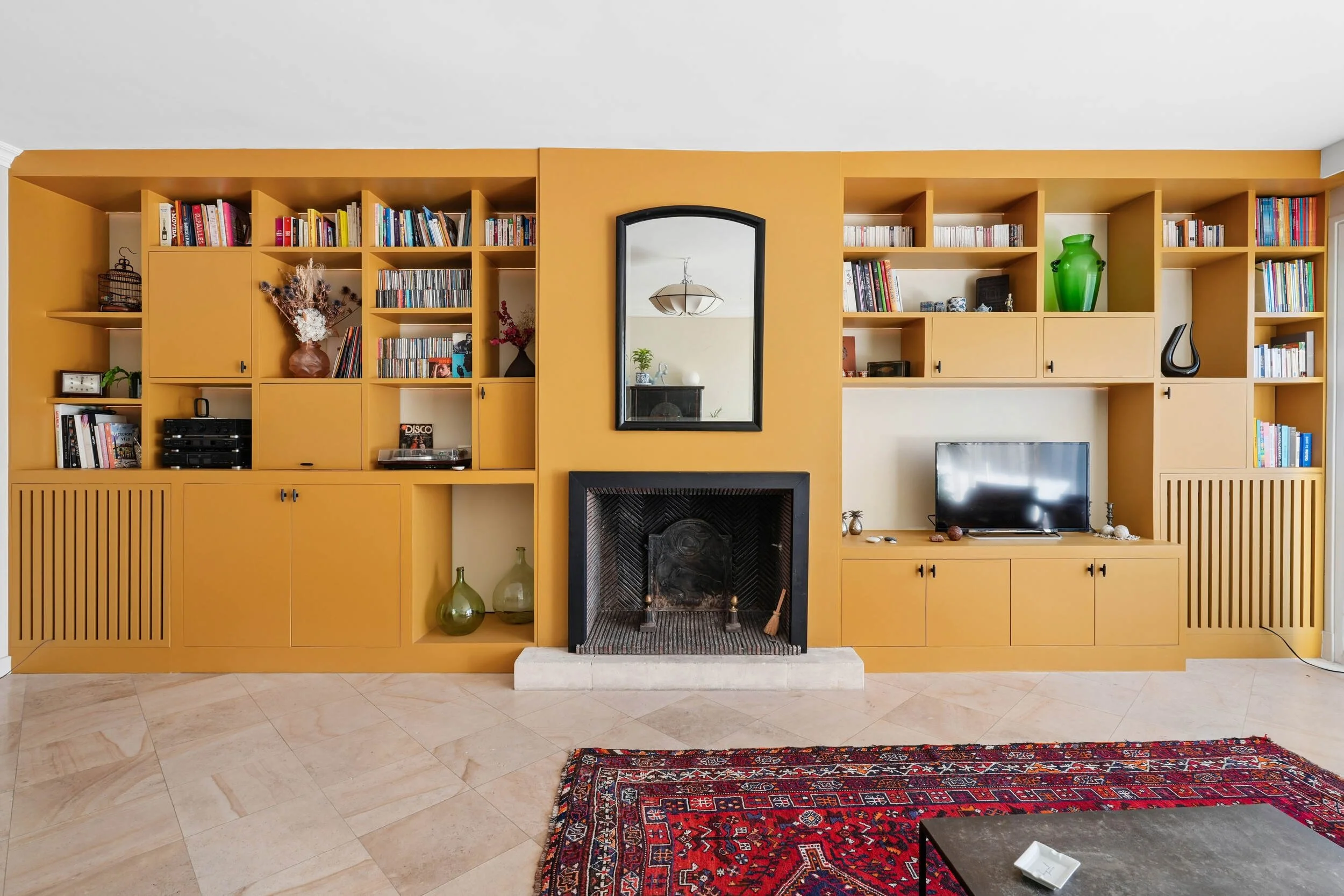 Grand meuble bibliothèque et TV sur mesure de couleur ocre, intégrant une cheminée réhabilitée dans un séjour à Colombes.