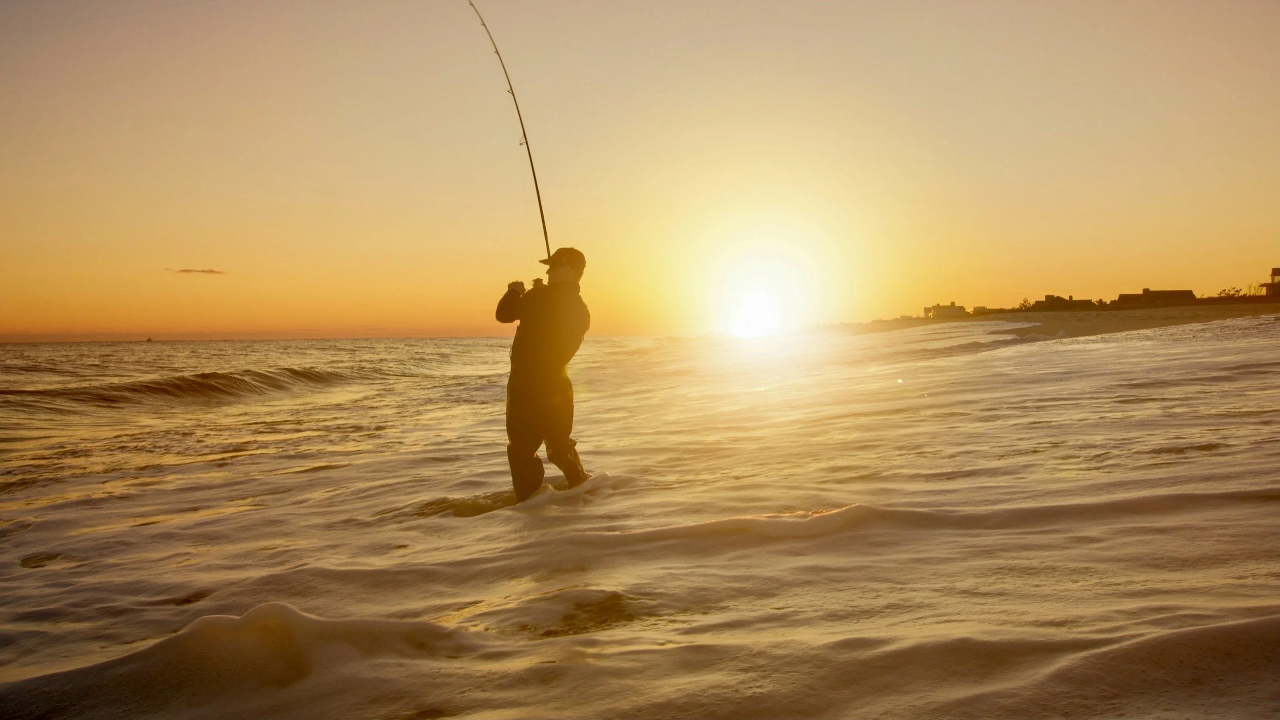 Person fishing in the ocean during sunset.