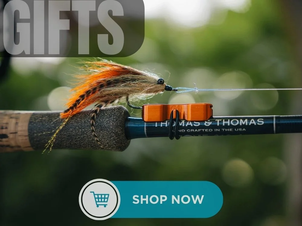 Close-up of a fishing rod with a fly fishing lure attached. The background is blurred greenery. The image includes a "SHOP NOW" button with a shopping cart icon.