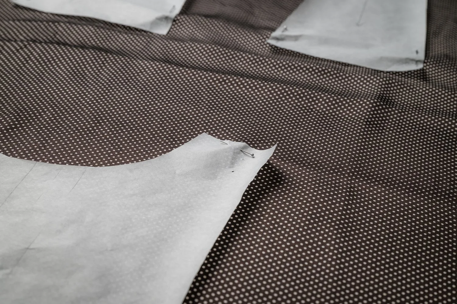 Nähen eines Stoffmusters mit weißen Punkten auf braunem Hintergrund, mit Nähte und Papierschnittmuster, einige Sicherheitsnadeln befestigen das Papier am Stoff.