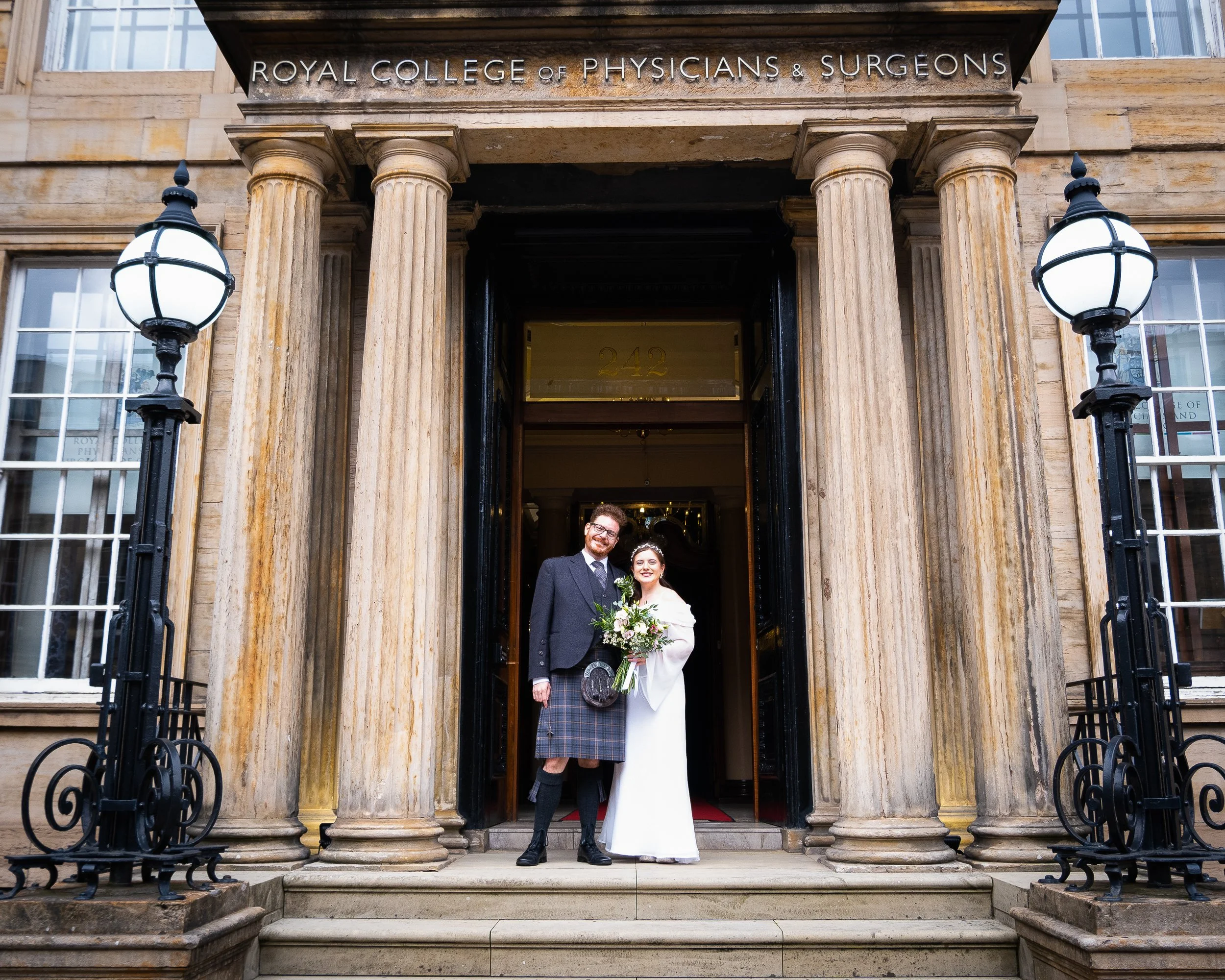 A bride and groom standing on the steps of the Royal College of Physicians & Surgeons, smiling for a wedding photo.