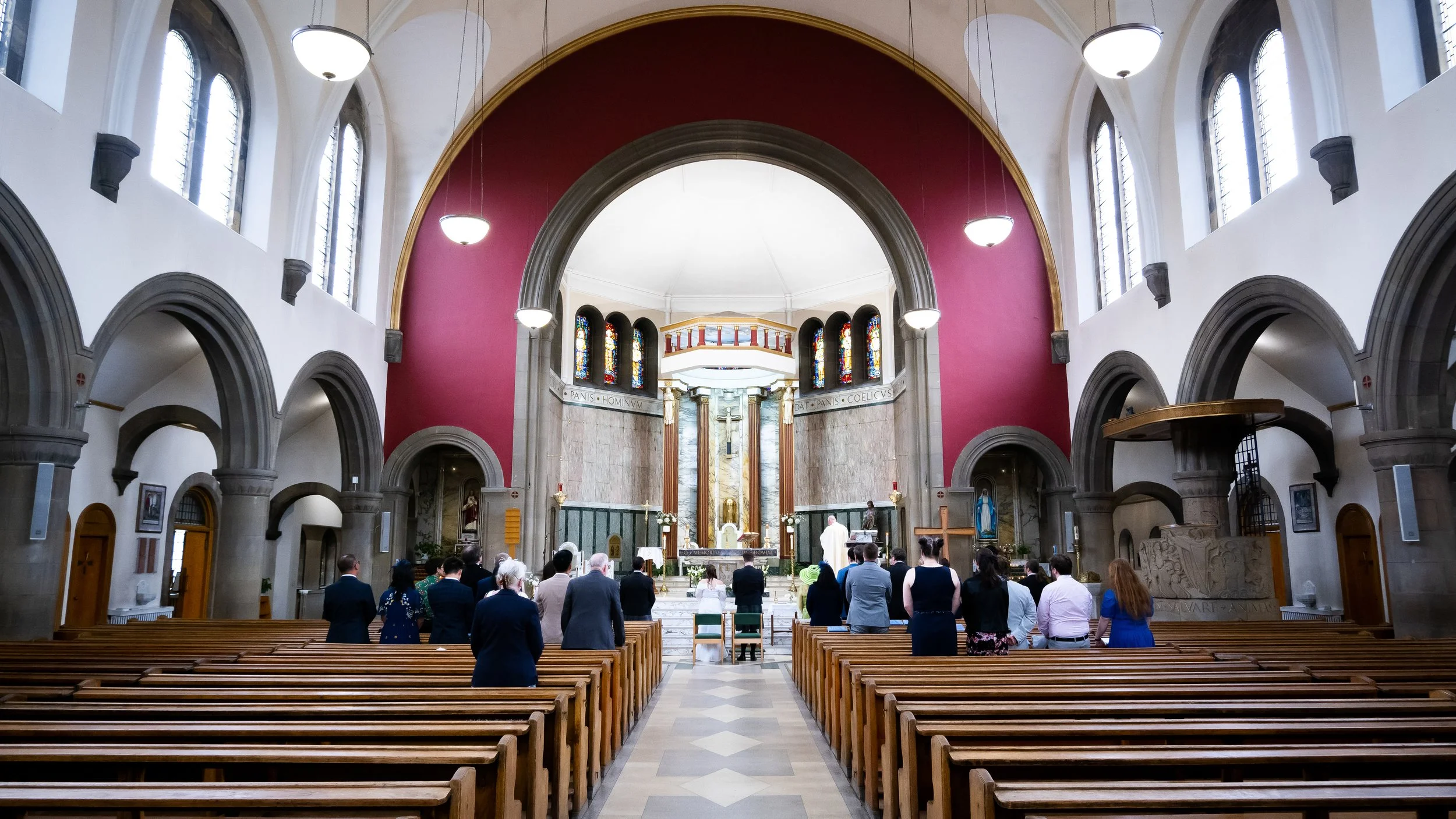 People gathered inside a church for a ceremony, standing in front of the altar with a priest, during a wedding or religious service.