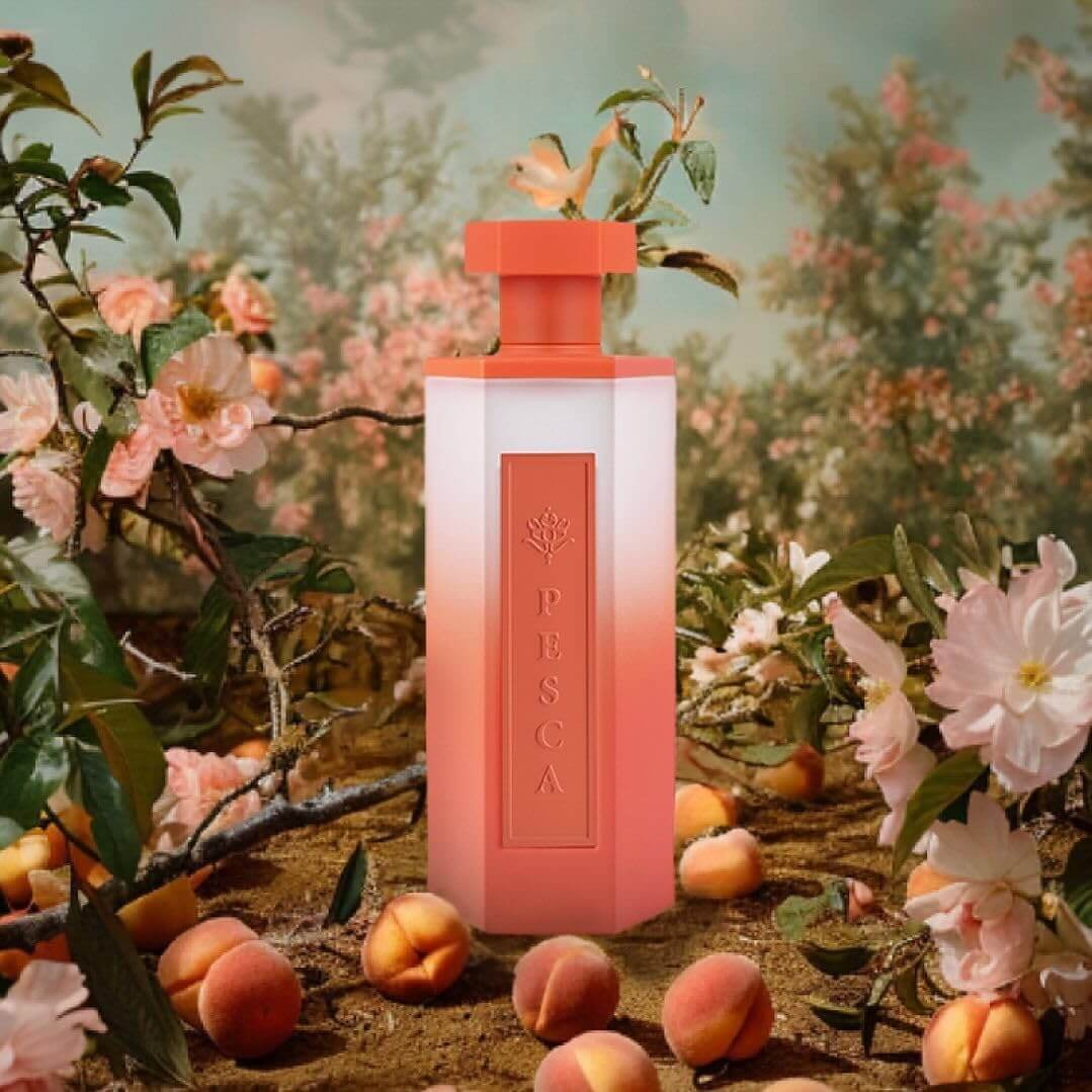 Pesca fragrance bottle surrounded by fresh peach slices, iris petals, and maté leaves on colourful background