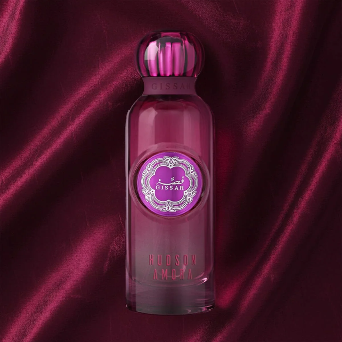 Gissah Hudson Amora EDP displayed against red-purple curtain backdrop, high-end floral-woody fragrance