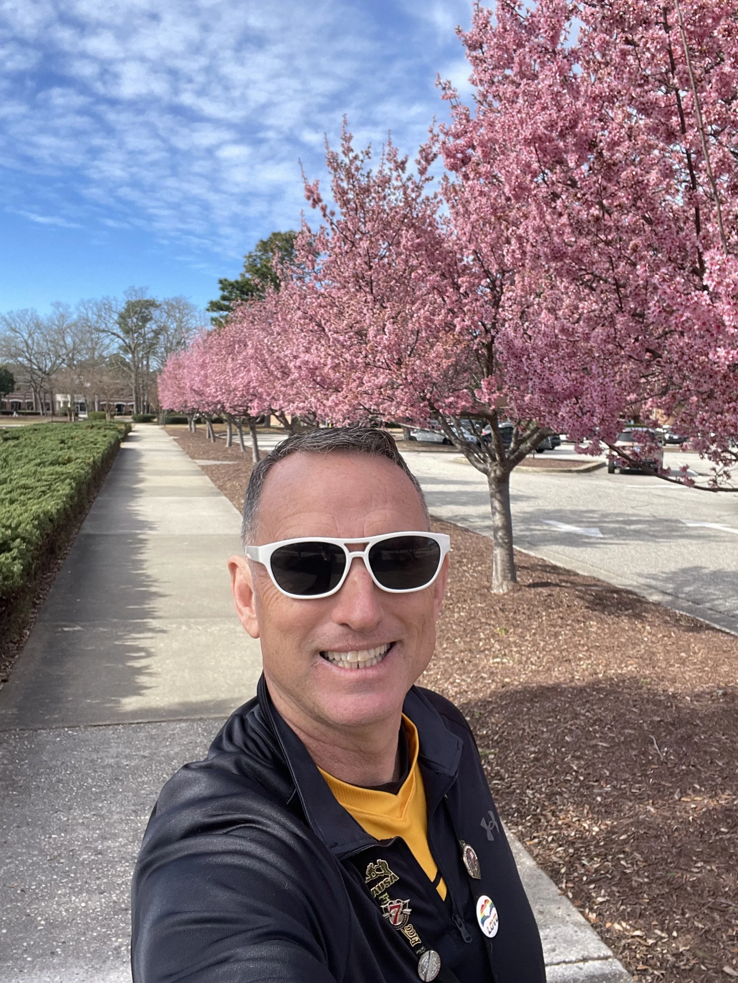 A person in a military uniform standing with arms open behind a table set for a religious service, including a cloth, book, chalice, and small bottles. The setting is a dimly lit room or warehouse.