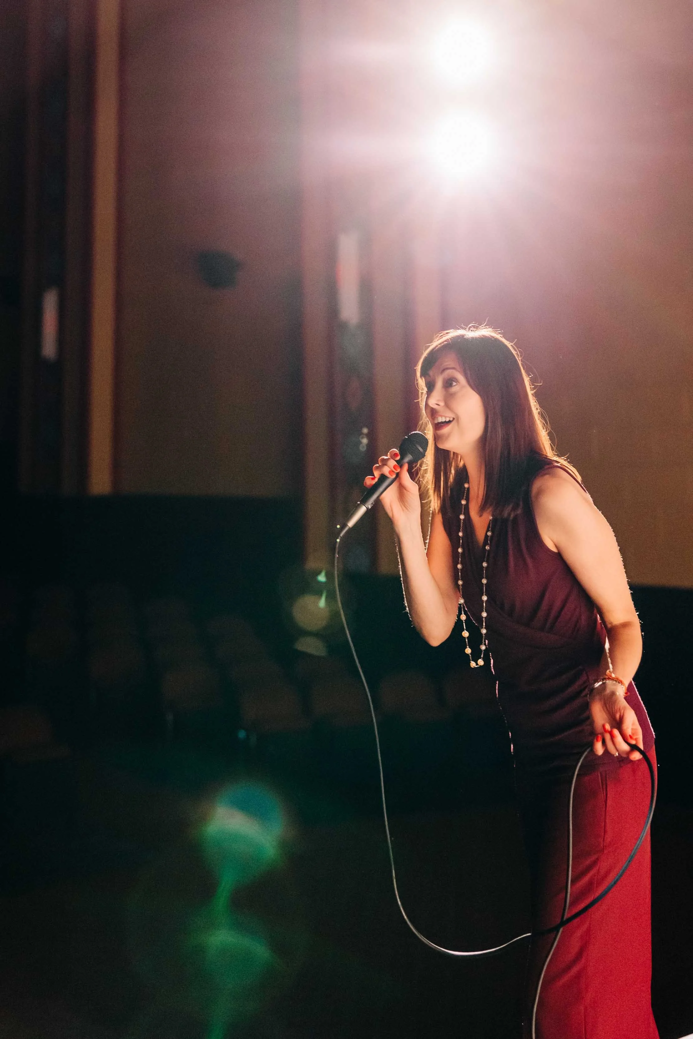 A woman singing into a microphone on stage with a bright light shining behind her, creating lens flare effects.