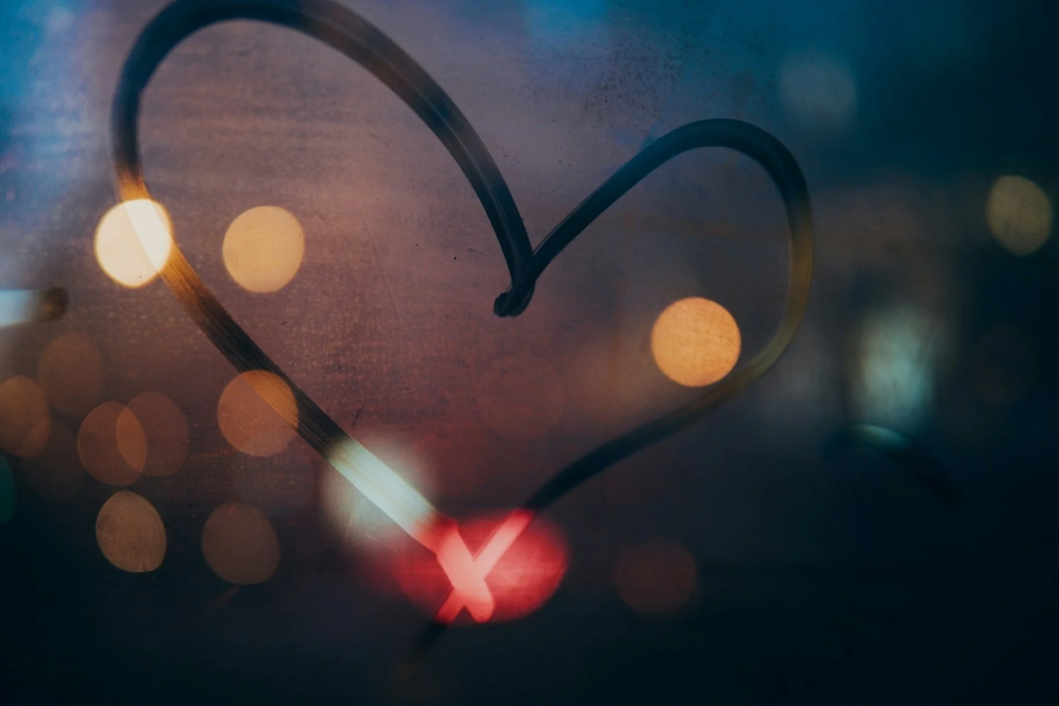A close-up of a clock with heart-shaped reflection on the glass, featuring blurred city lights in the background at night, creating a romantic atmosphere.