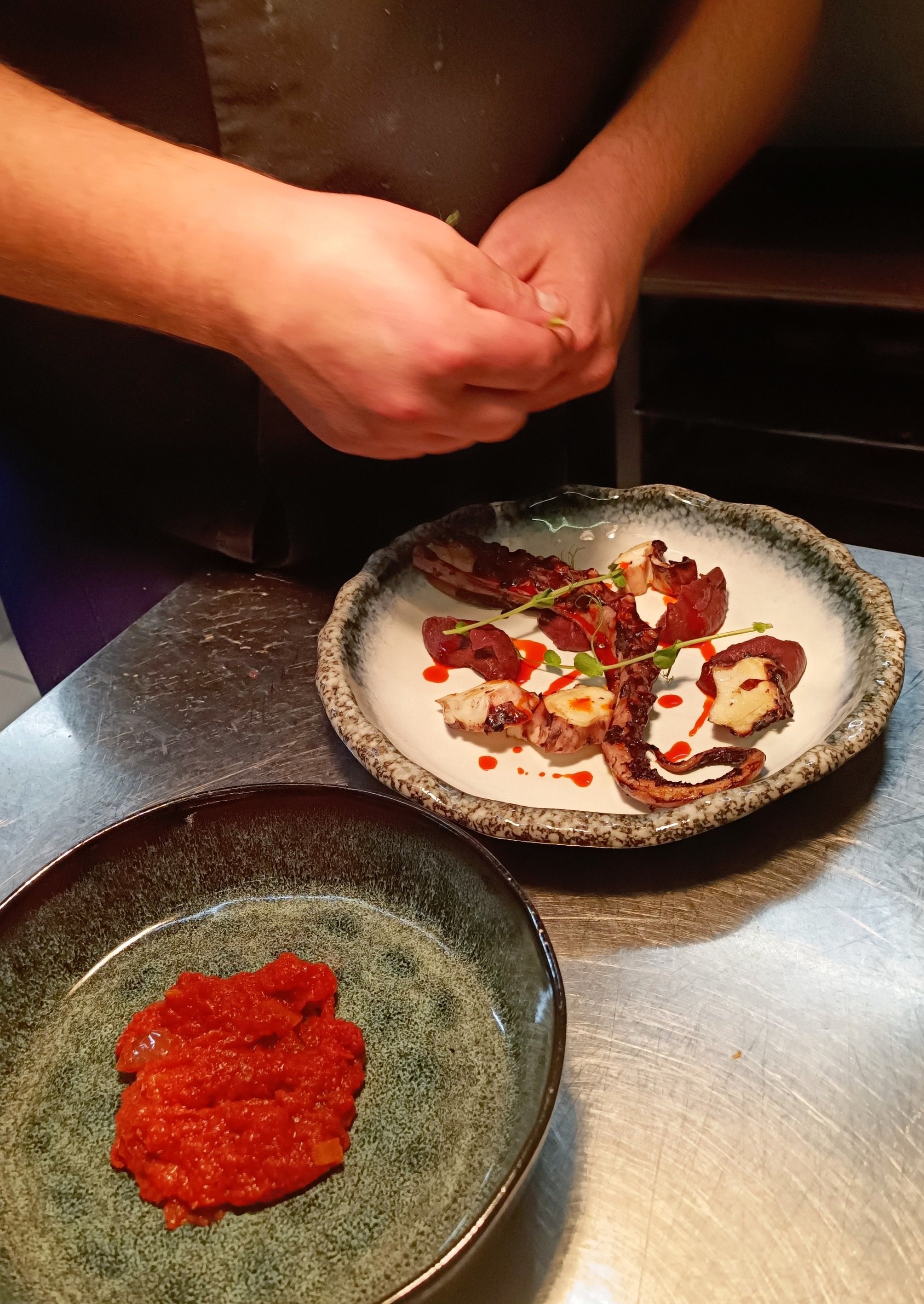 Chef en préparation d'un plat de pieuvre grillée avec sauce tomate rouge et herbes fraîches.
