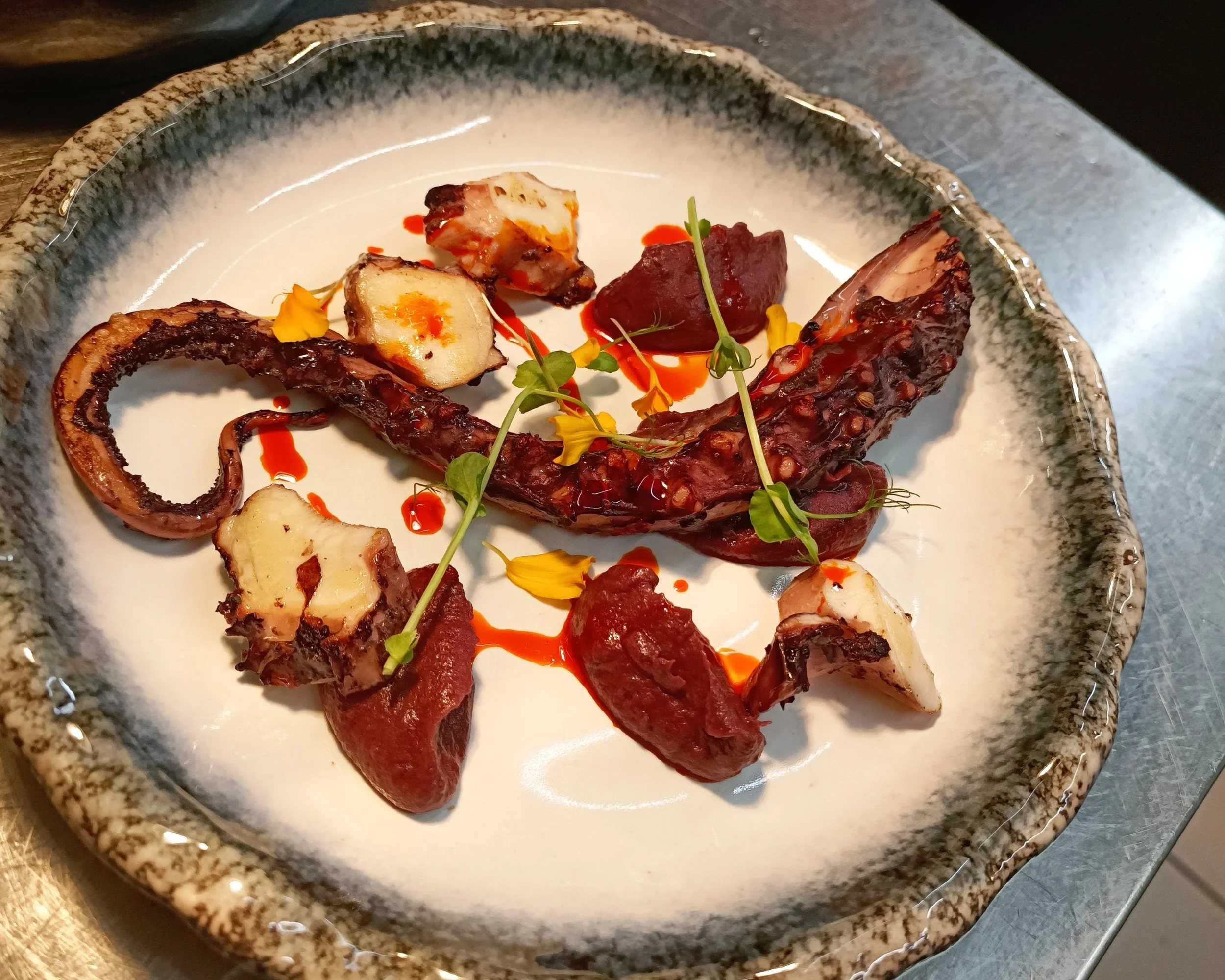 Assiette de tentacule de poulpe grillé, herbes fraîches et fleurs jaunes, avec une sauce rouge épicée à la Spianata.