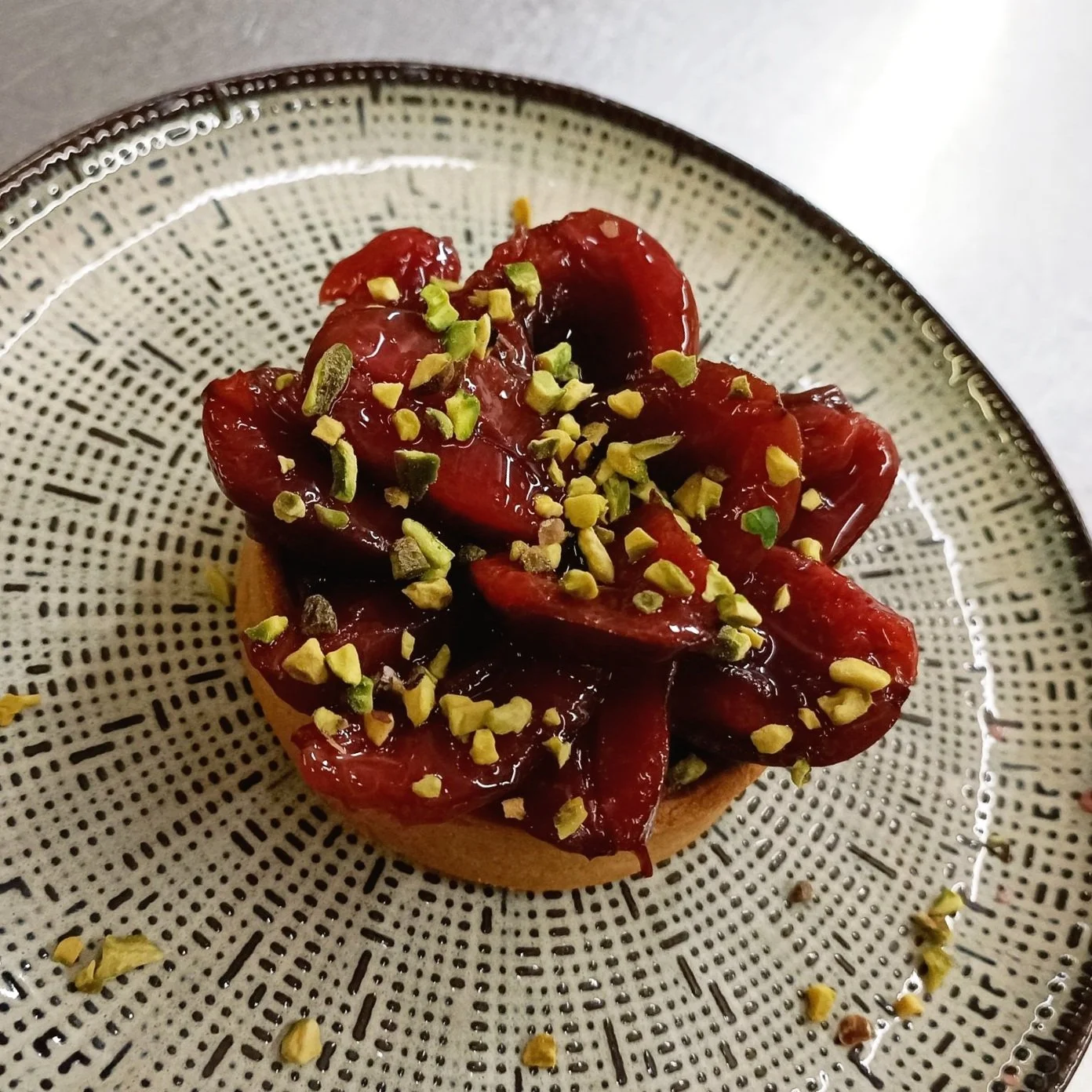 Tarte garnie de fruits rouges et de pistaches sur une assiette décorative.