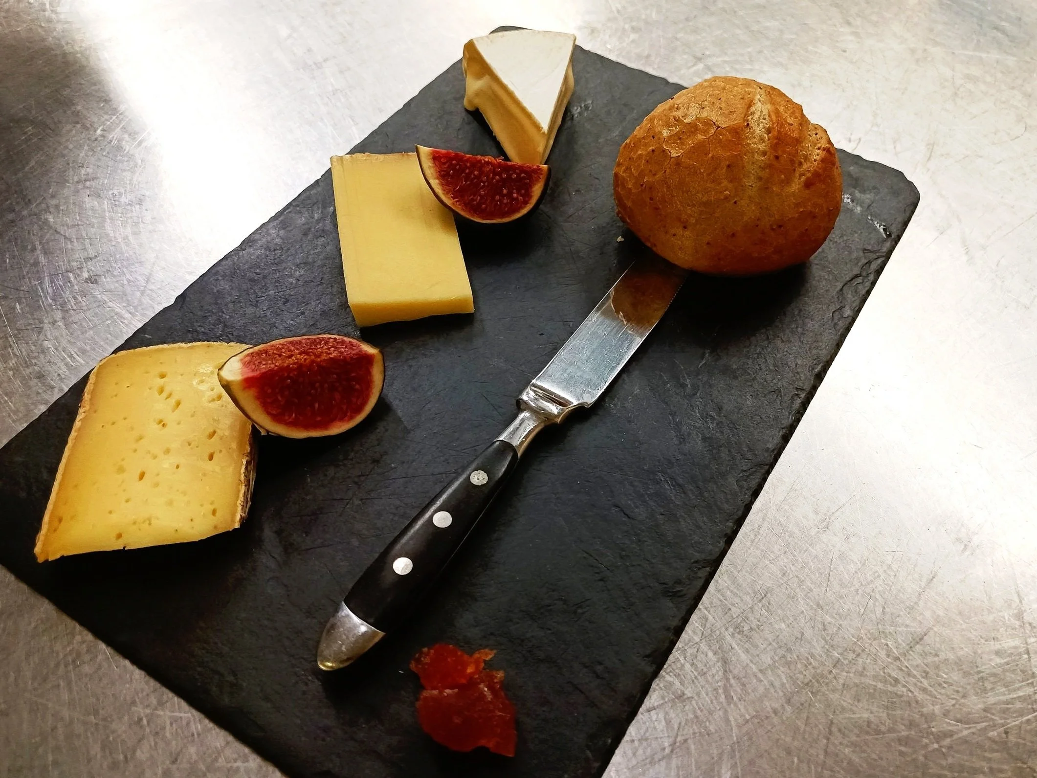 Assiette de fromage avec figues, couteau, petit pain sur une ardoise.