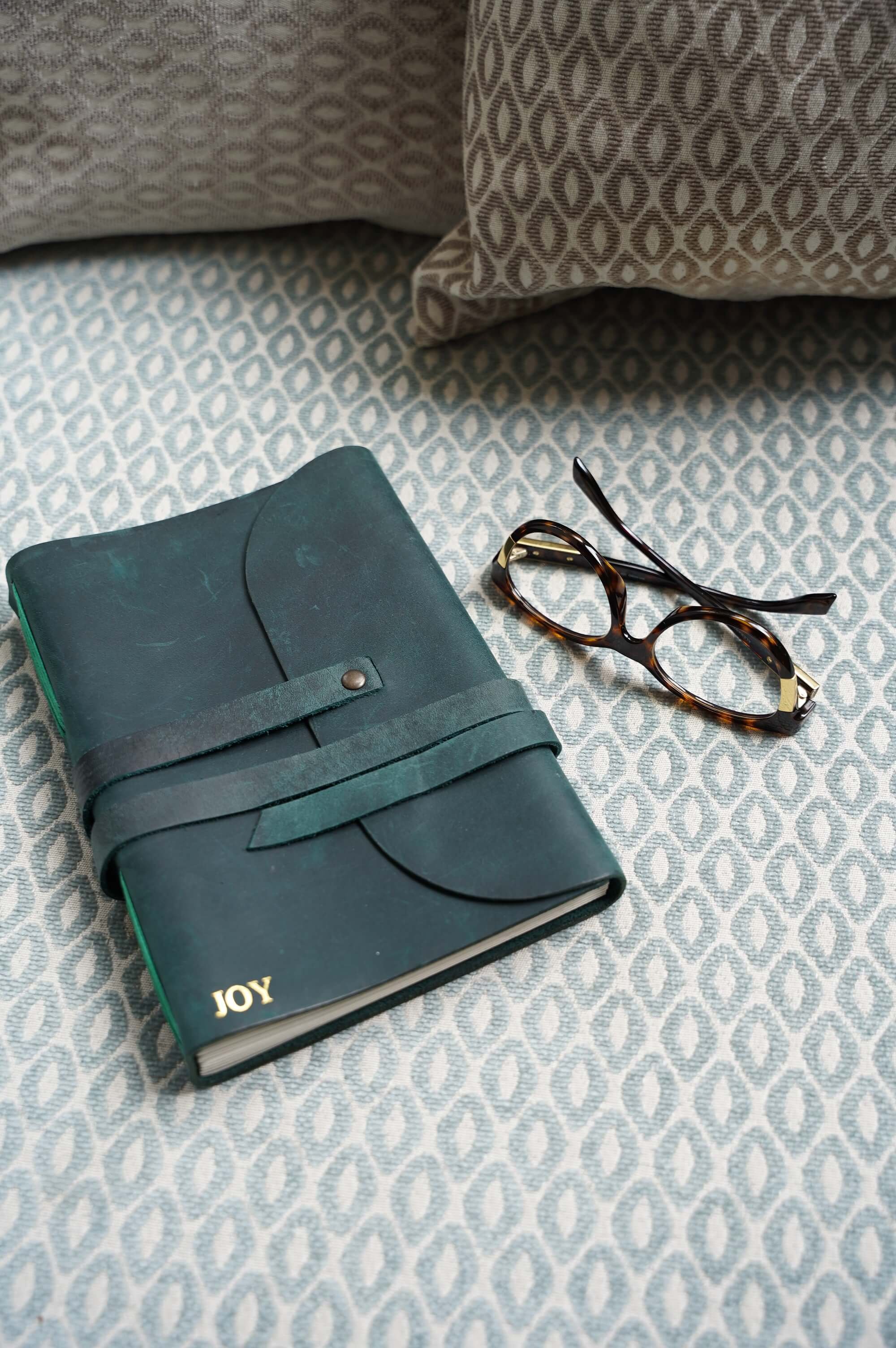 Blue leather journal with "JOY" inscription and tortoiseshell glasses on patterned fabric. help for sleepless nights.