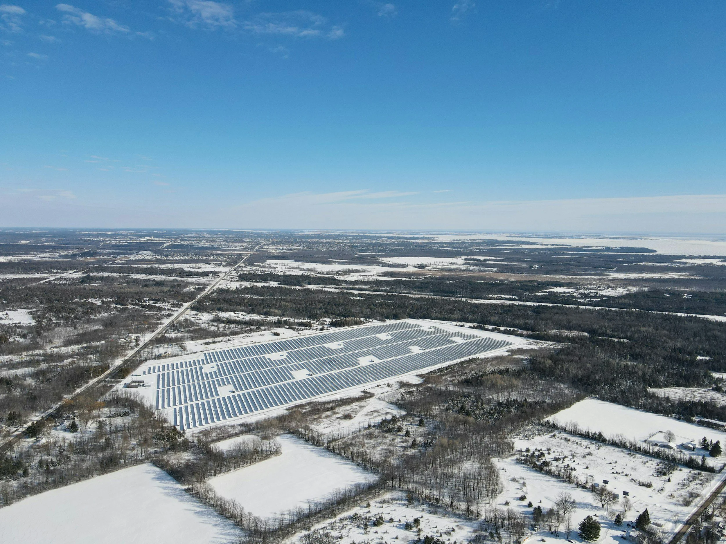 An aerial view of multiple solar panel arrays arranged in rows on a grassy field.