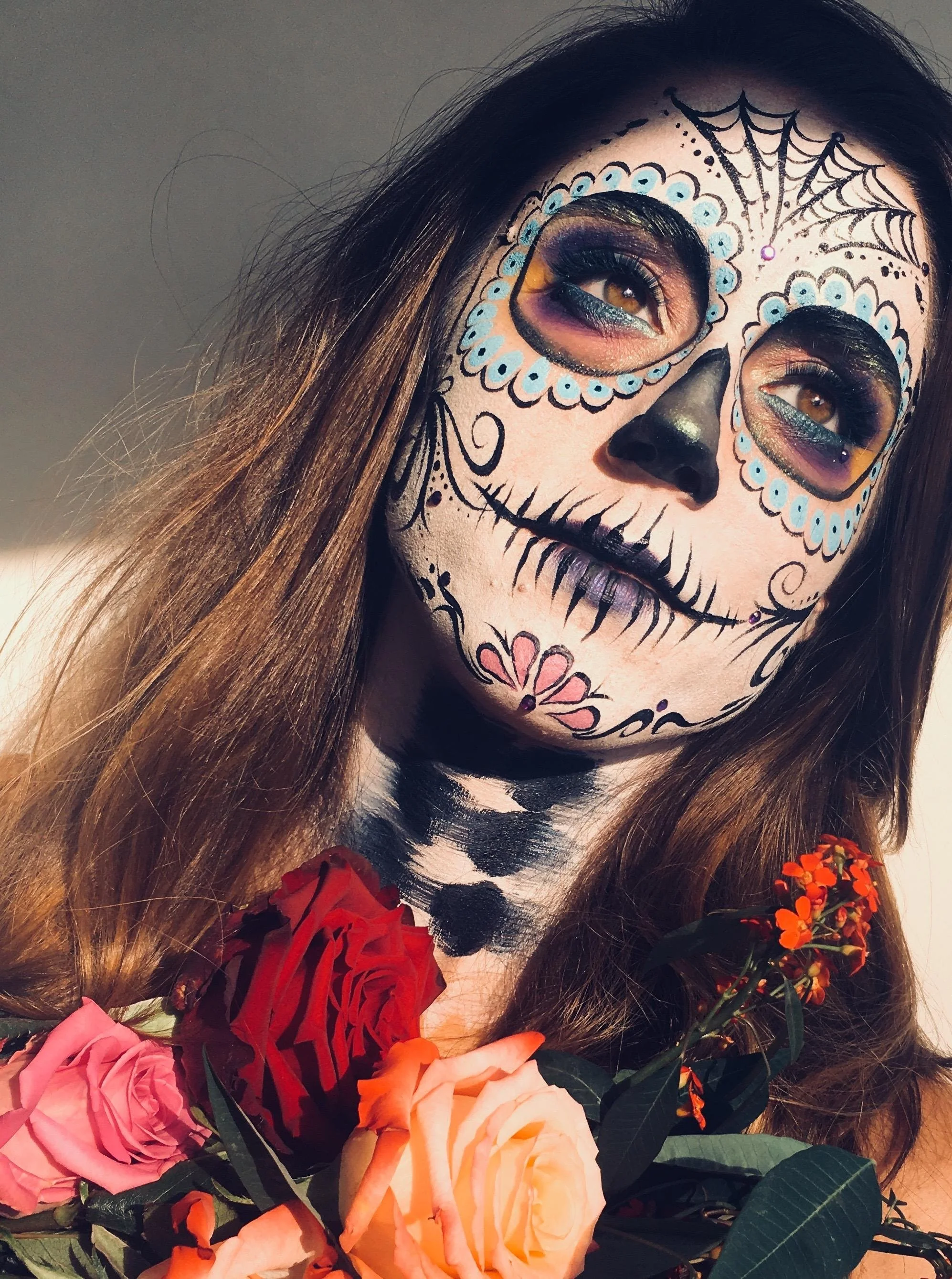 Person with sugar skull face paint holding colorful flowers.