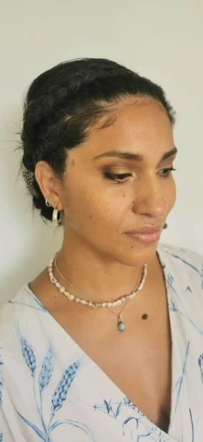 Woman with braided hair, wearing earrings and necklaces, in a light floral top.