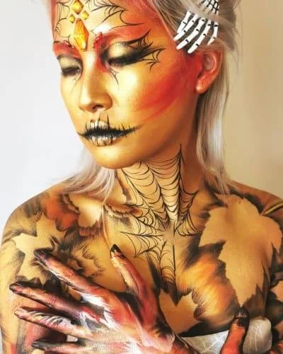 Person with artistic Halloween makeup featuring spiderweb and skeleton effects on face and body