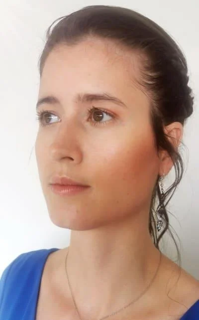 Woman wearing blue shirt with earrings, looking to the side.