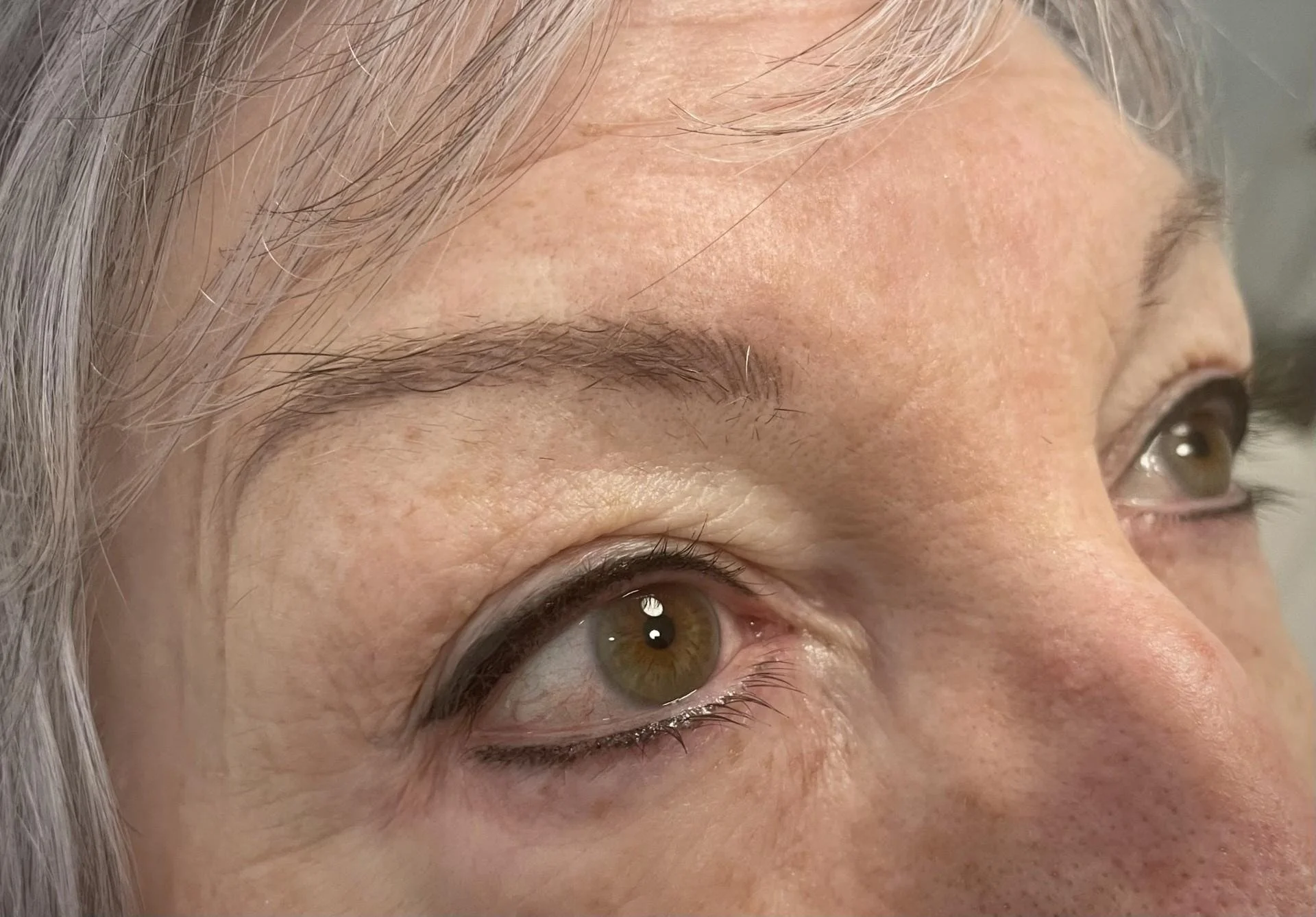 Close-up of an older person's eyes with light-colored irises, visible wrinkles, and gray hair.
