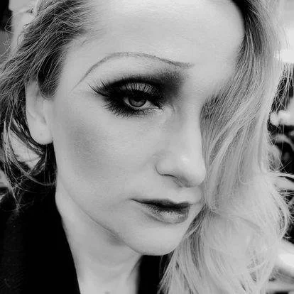 Black and white photo of a person with dramatic makeup and wavy hair style.