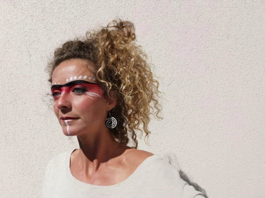 Person with curly hair and creative face paint against a plain background