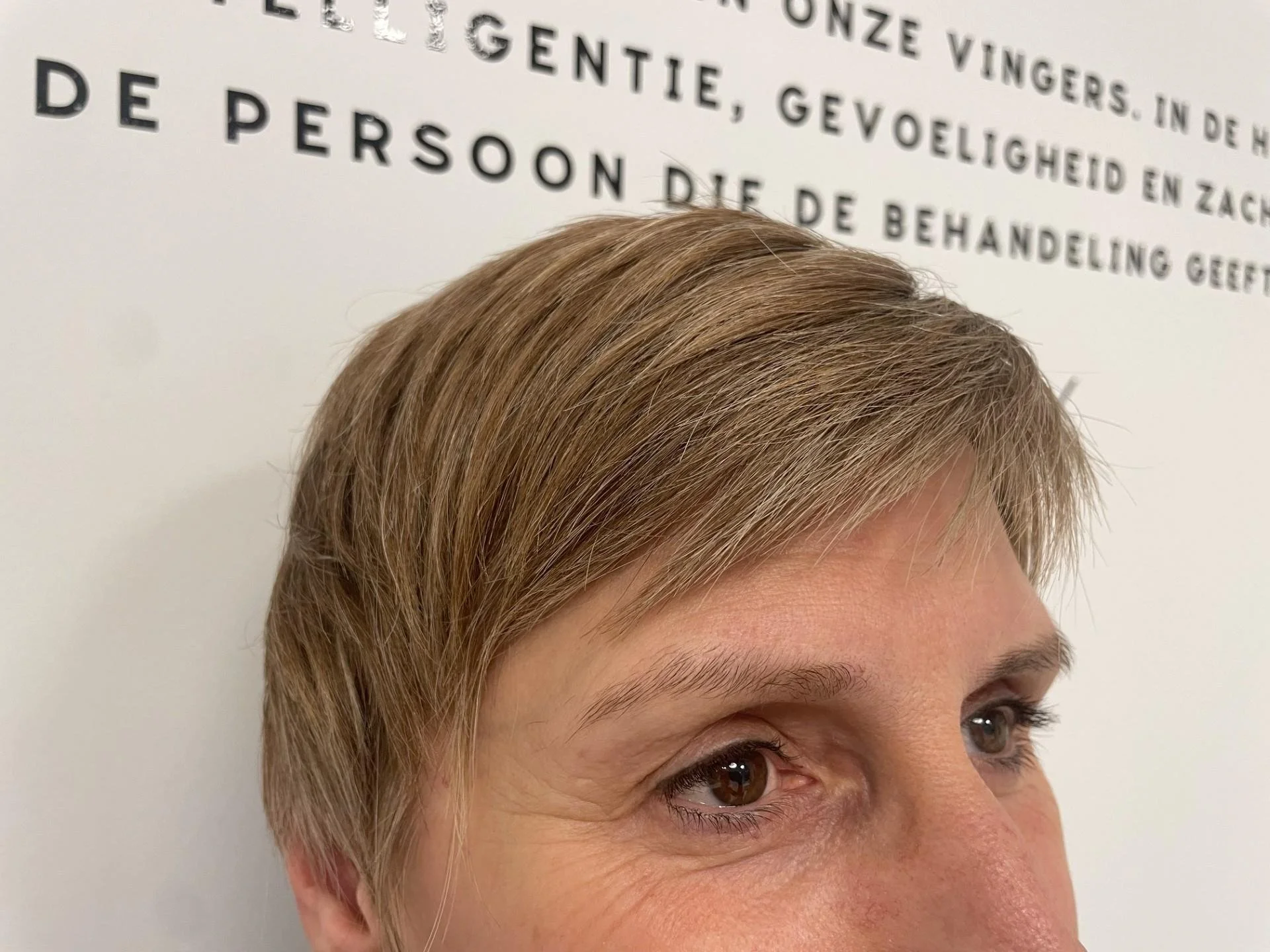 Close-up of a person's short blonde hair and eyes against a wall with text in a foreign language.