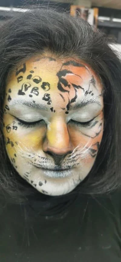 Person with intricate animal face paint resembling a leopard or big cat, with closed eyes.
