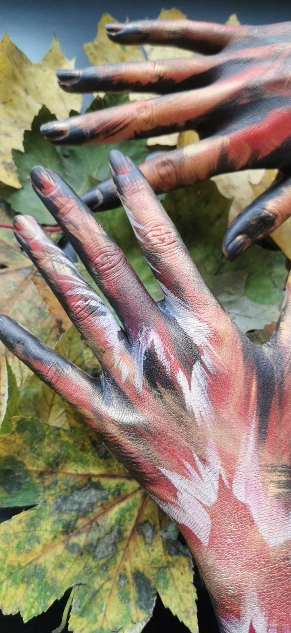 Hands with artistic paint over autumn leaves.
