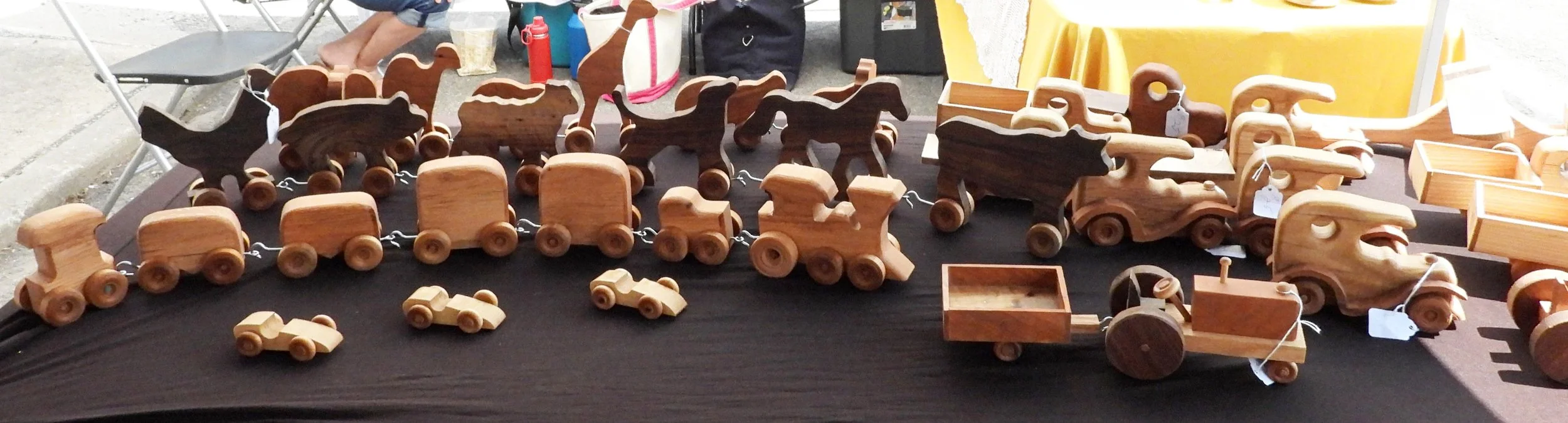 Wooden trains and animal figures displayed on a table at a craft fair.